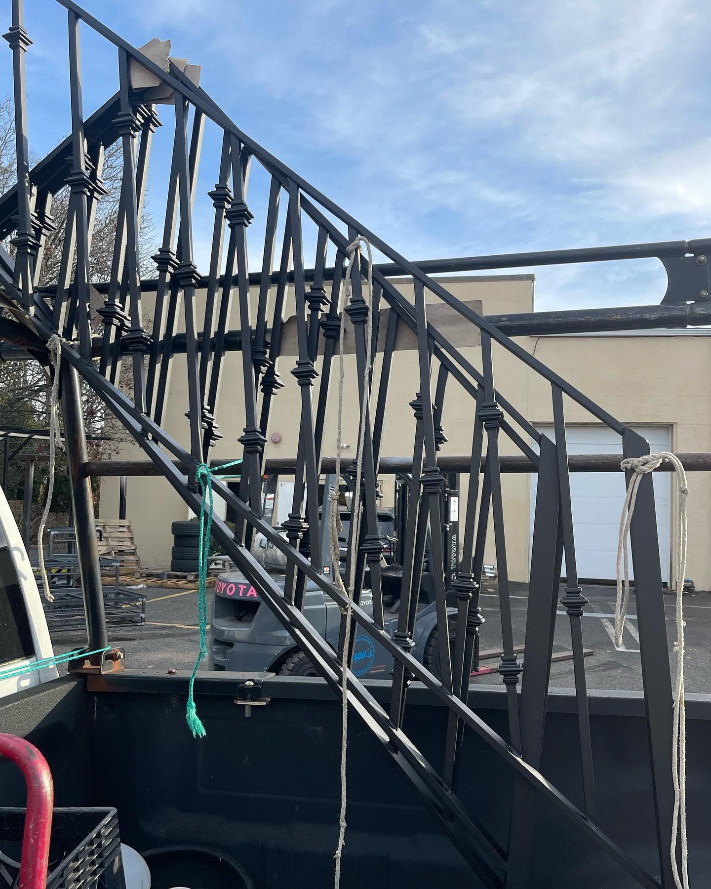 Black metal railings for stairs loaded onto the back of a truck, viewed from the side in an outdoor parking lot.