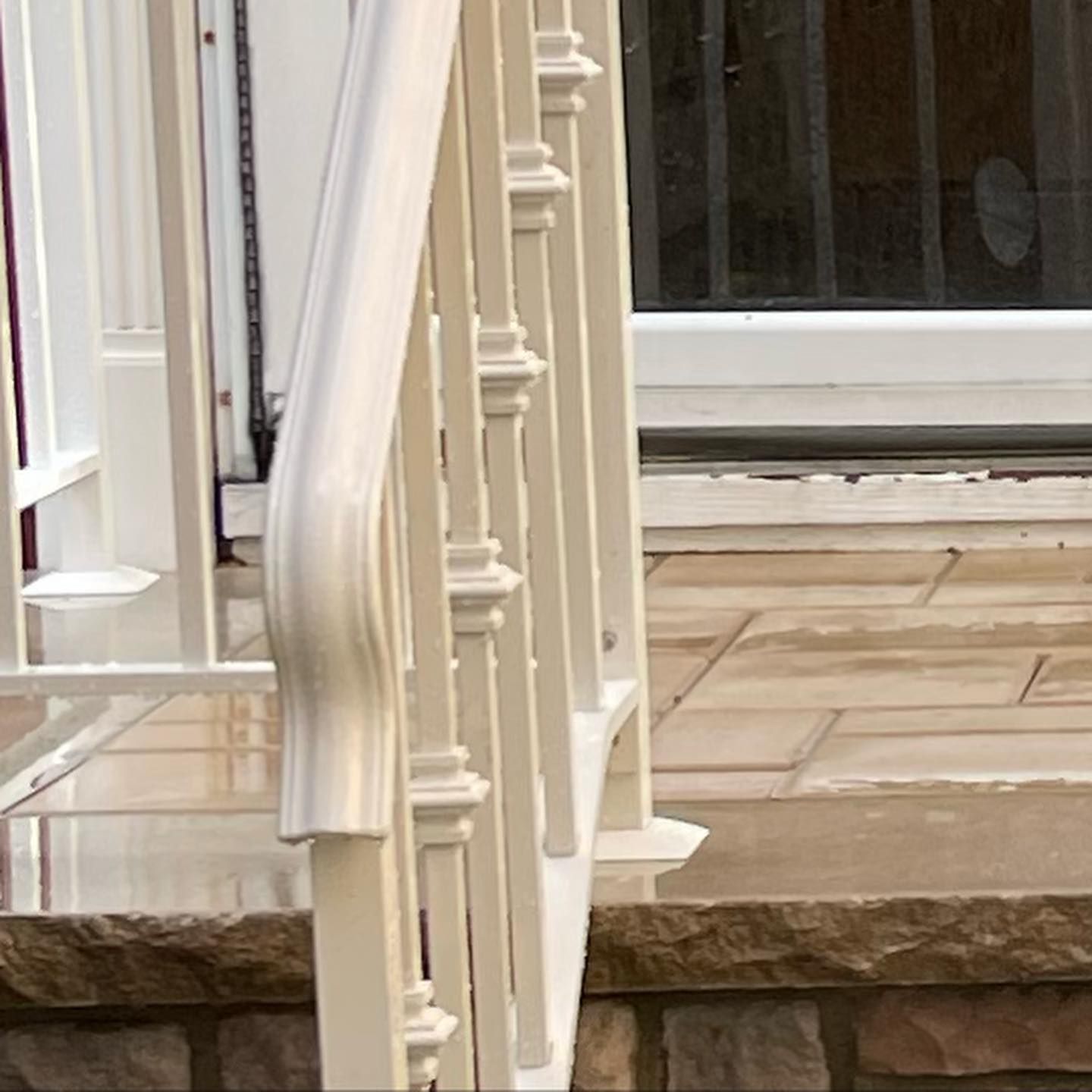 A close-up view of an off-white metal railing and decorative balusters on a stone porch next to a glass door.