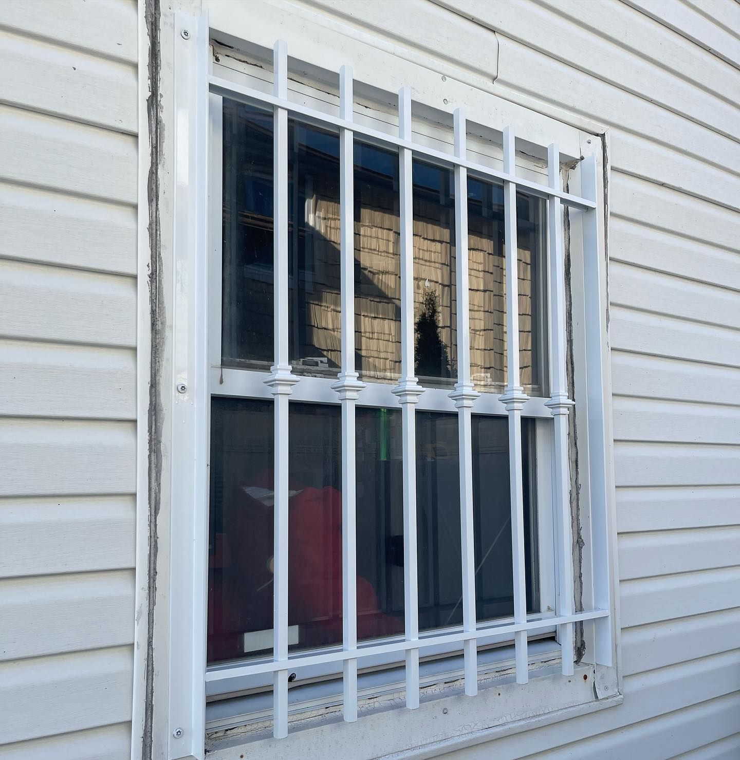 White metal security bars are installed over a window on a light-colored, vinyl-sided building.