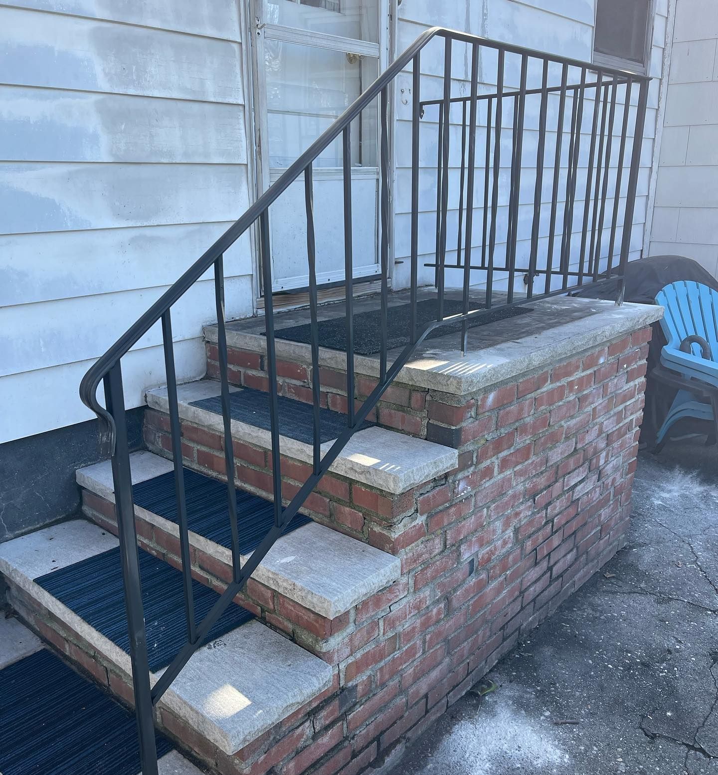 Outdoor brick steps with light stone treads and a black metal handrail leading to a white door.