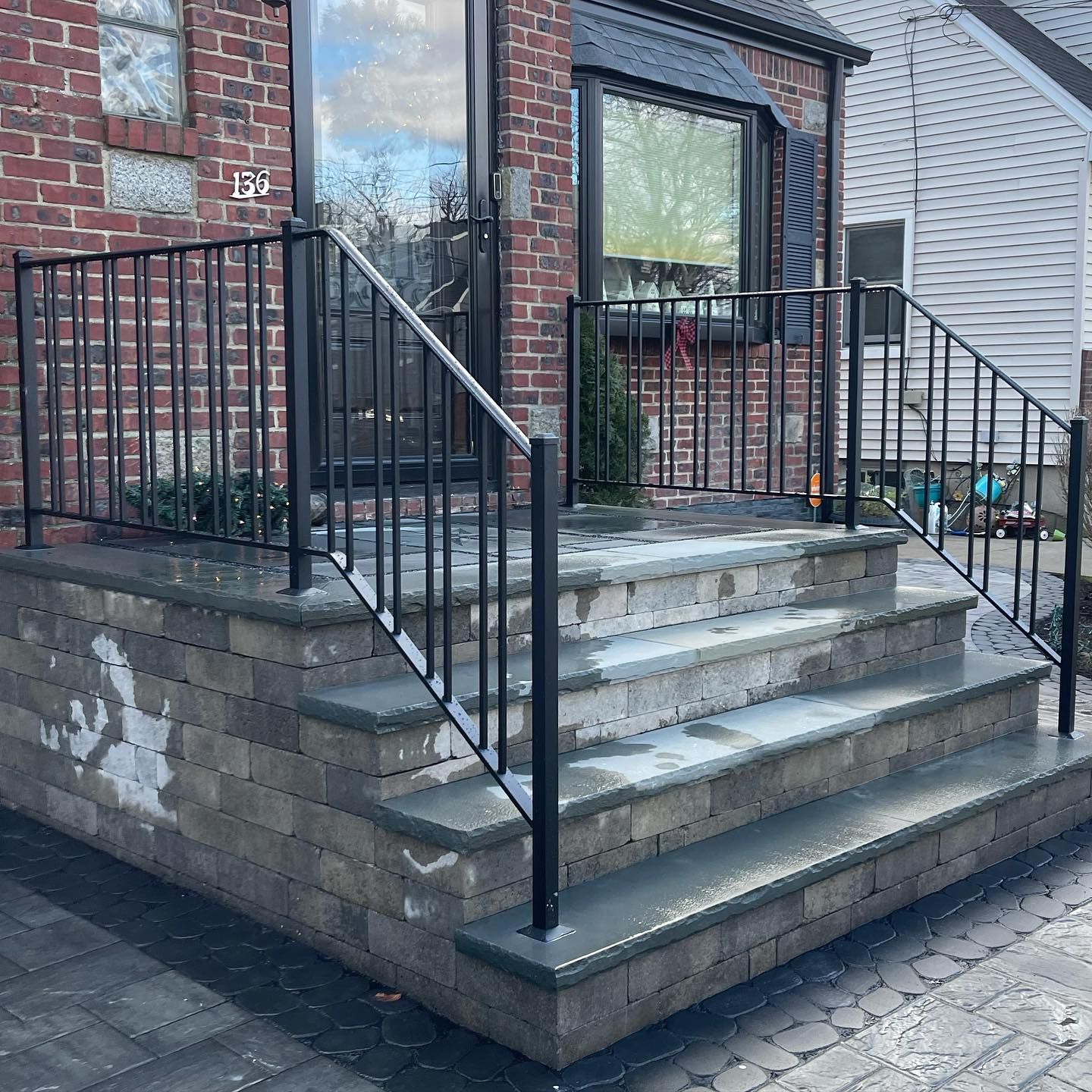 Stone steps with gray treads and a black metal railing lead to the front door of a brick house.