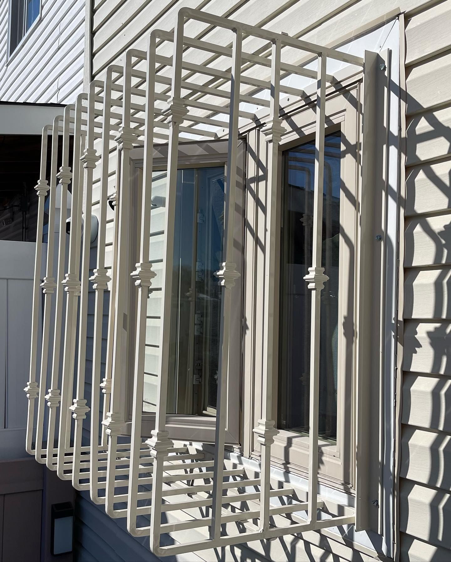 A white metal security cage or grille mounted over a basement window on a house with beige vinyl siding.