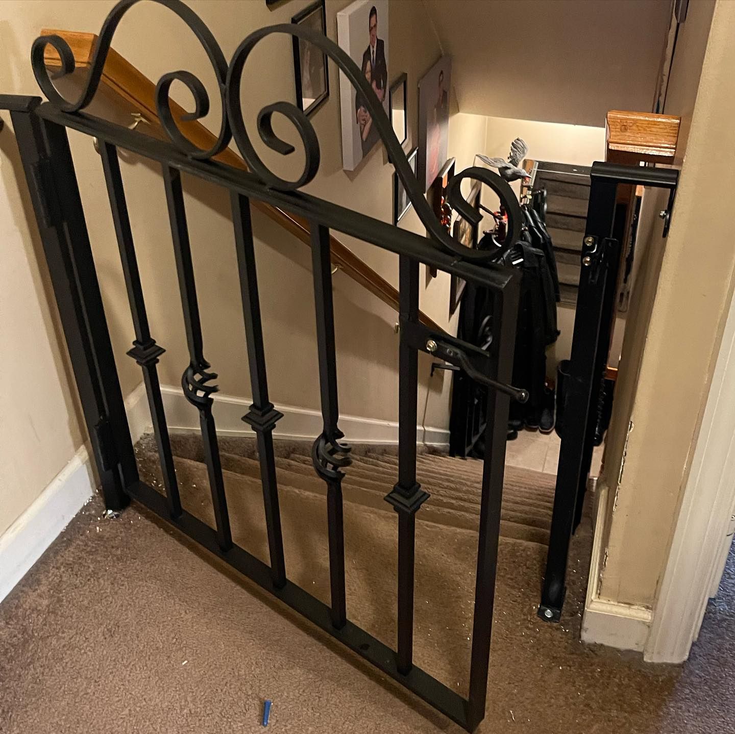 Black metal baby gate with decorative scrollwork installed at the top of a carpeted staircase.