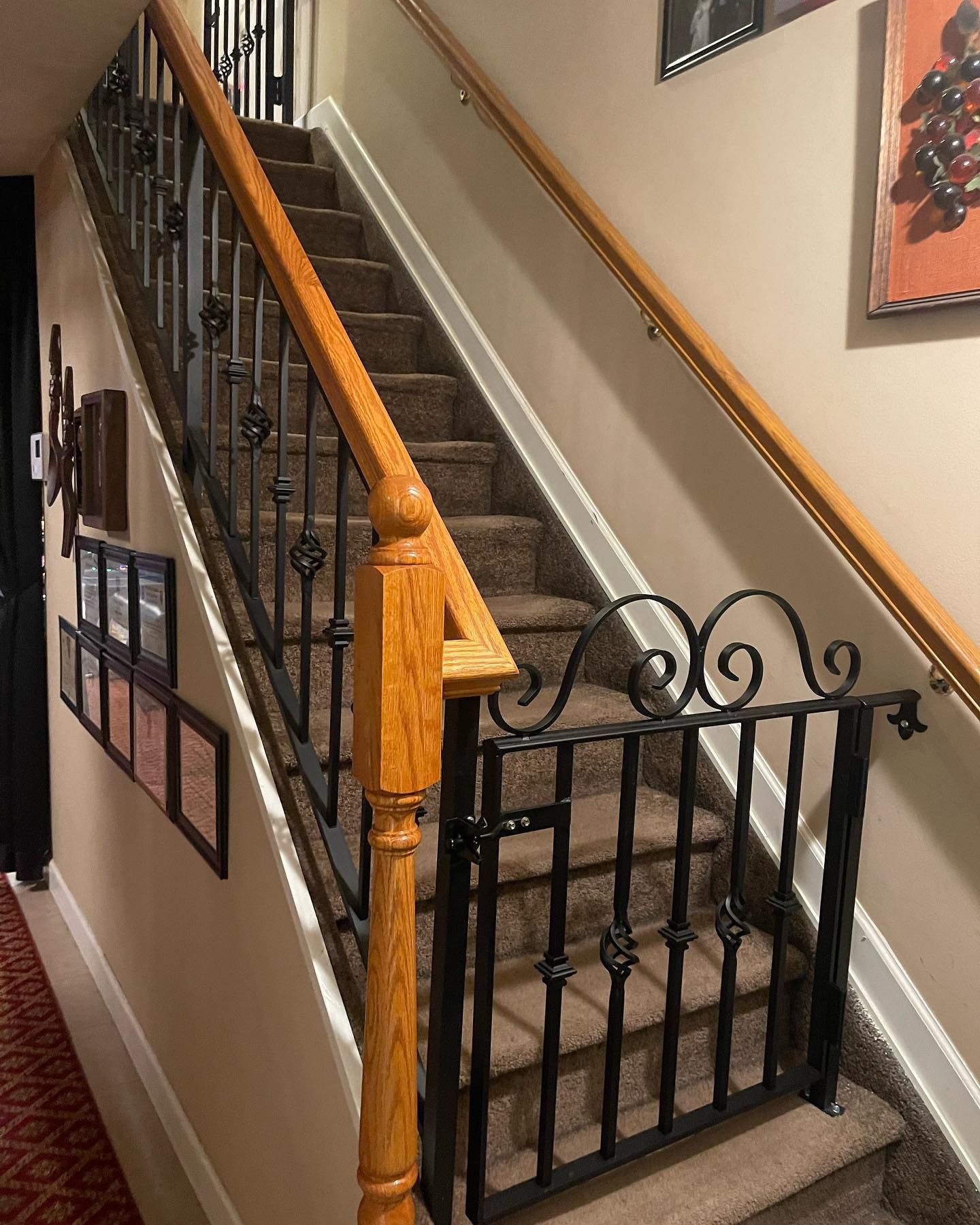 A carpeted staircase features a decorative black metal gate installed at the bottom, matching the iron railing.