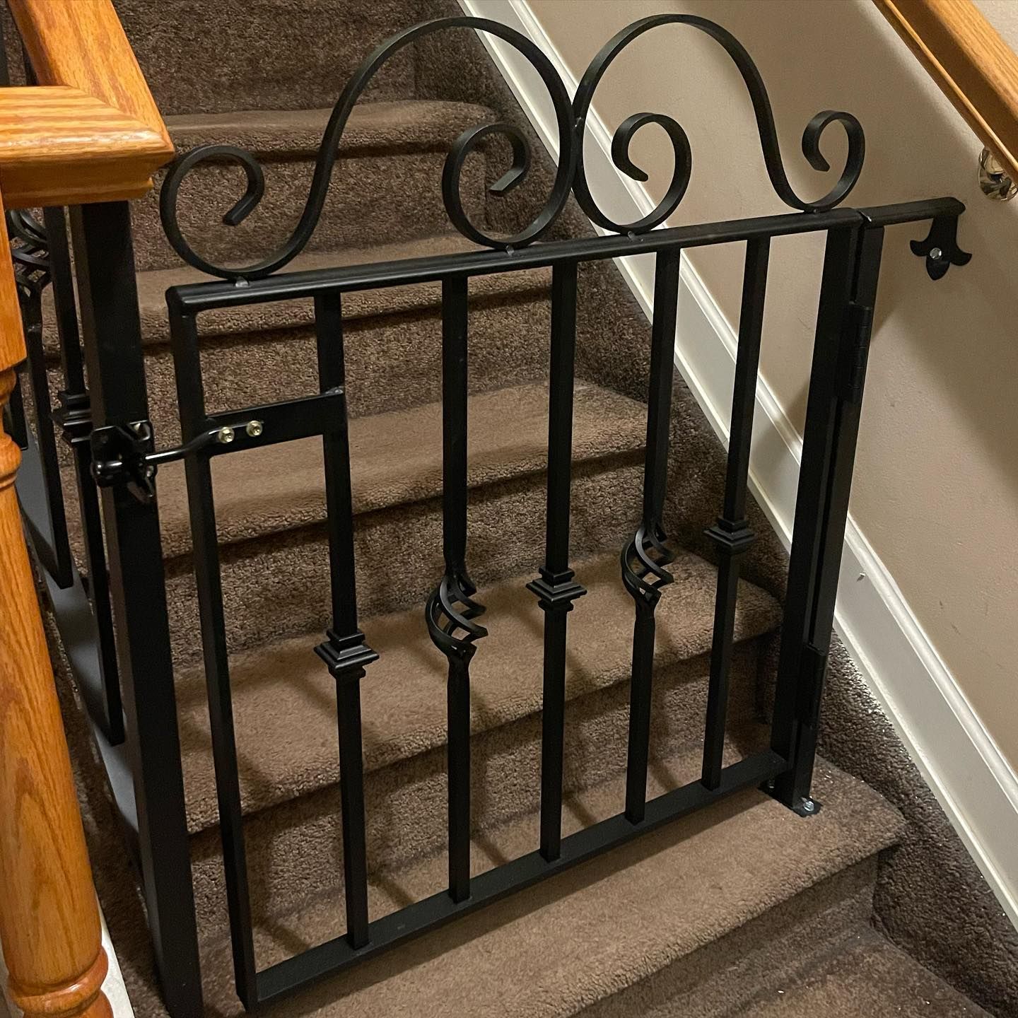 A black wrought-iron safety gate with decorative scrolls installed at the bottom of a carpeted staircase.