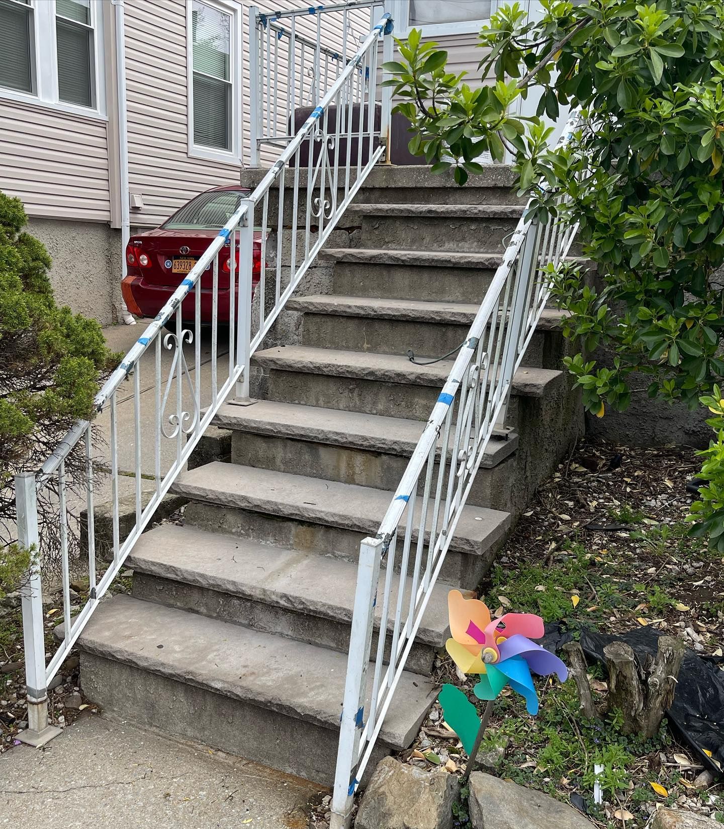A set of concrete outdoor stairs with white metal railings leading up to a residential building entrance.
