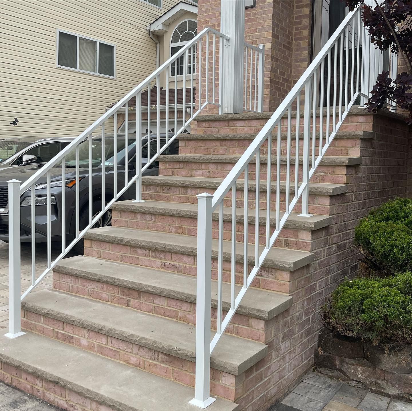White metal railings flanking a brick staircase leading to a building entrance next to a parked car.
