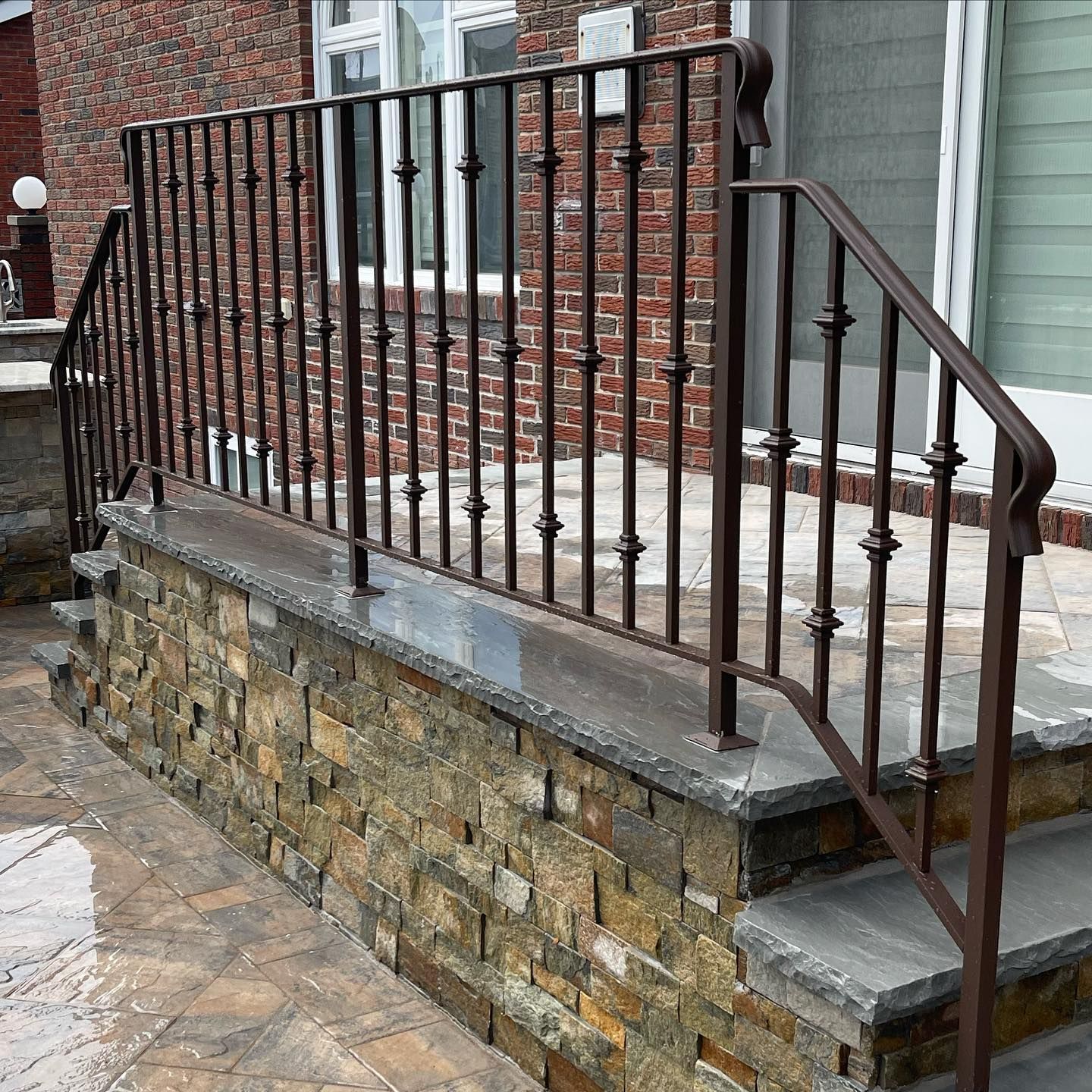 Brown metal railing on stone steps leading up to a brick house entrance.