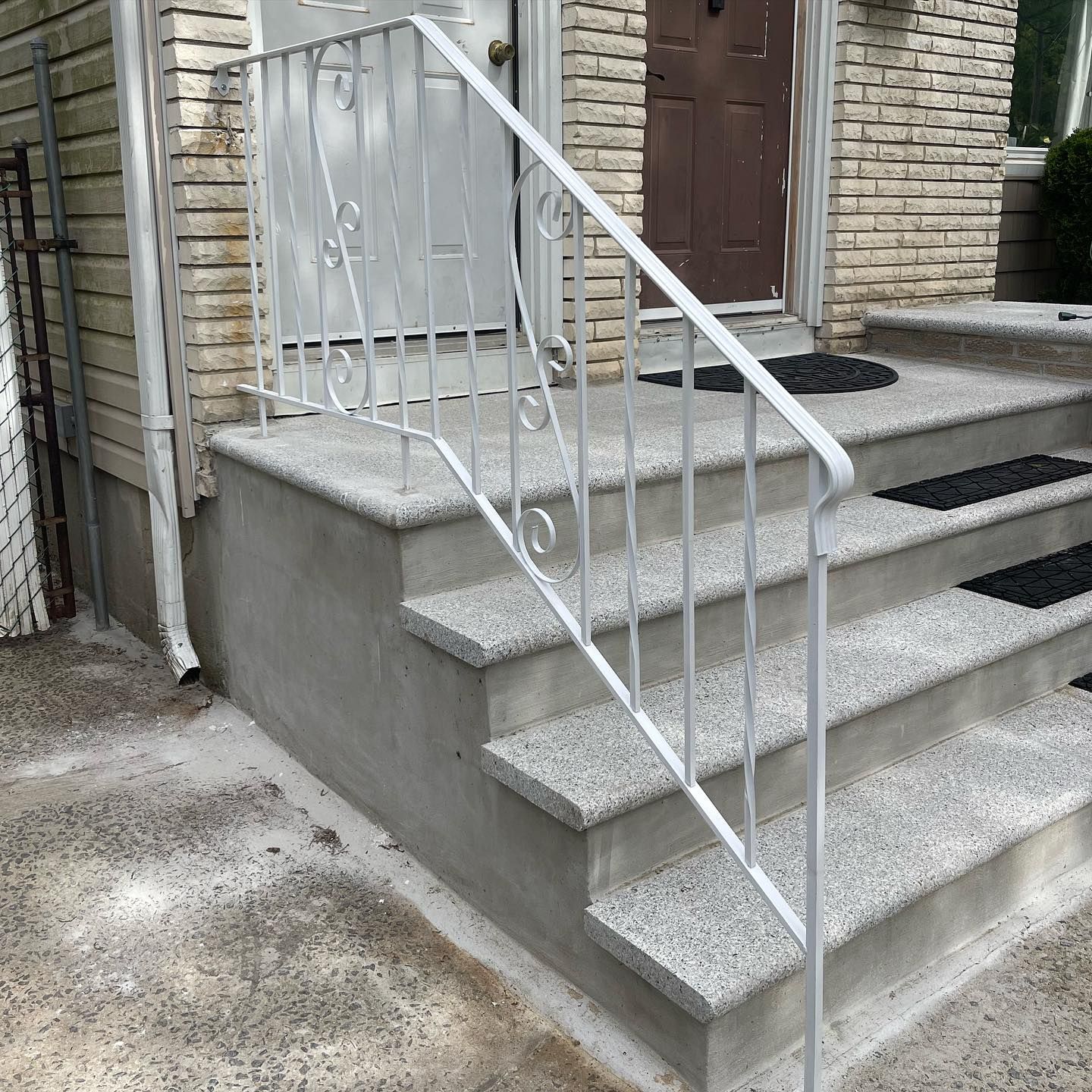 White metal railings on stone steps leading up to a brown door on a brick building.