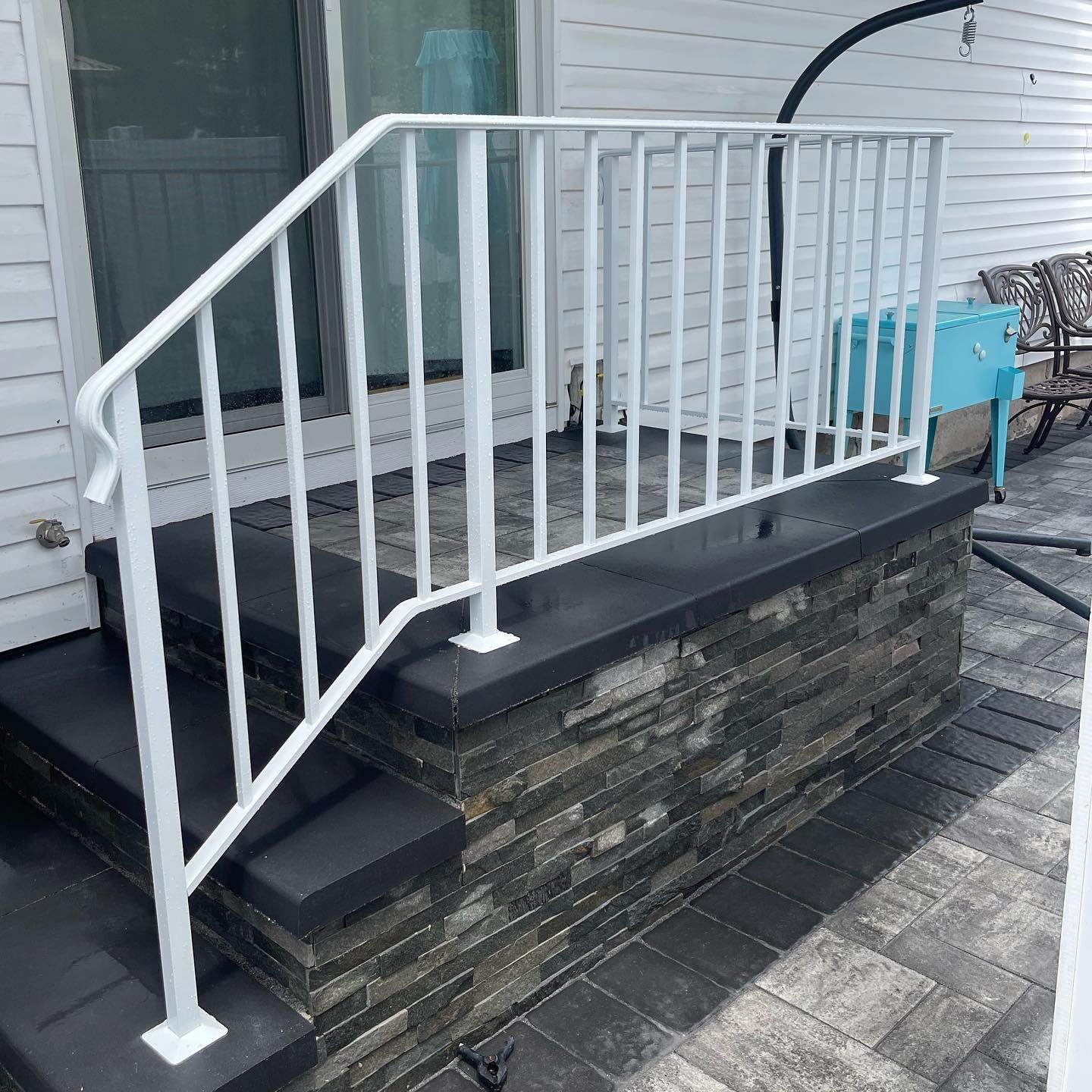A white aluminum railing attached to dark stone steps leading to a sliding glass door on a patio.