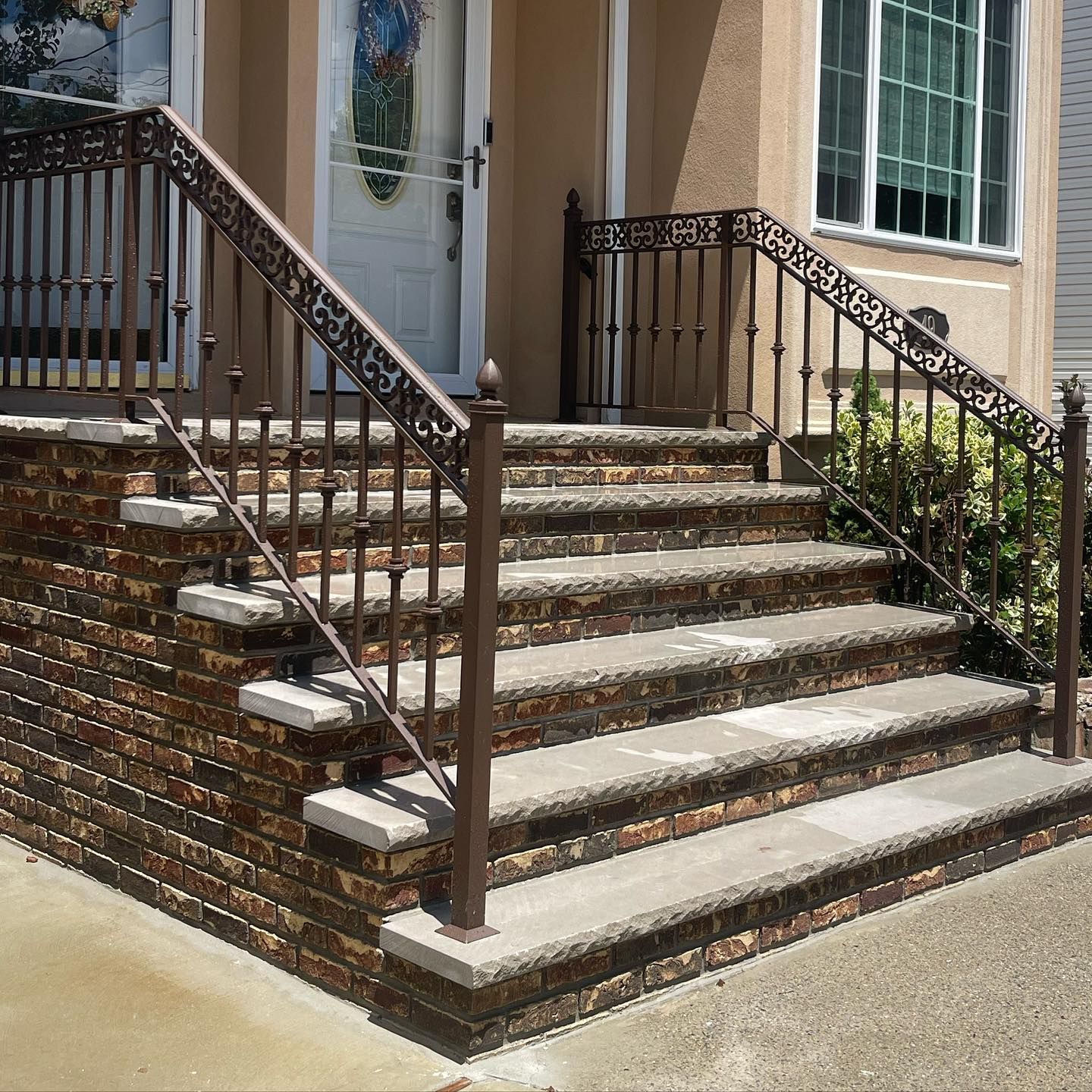 A set of stone steps leading to a house entrance, featuring dark metal railings and a textured brick side wall.