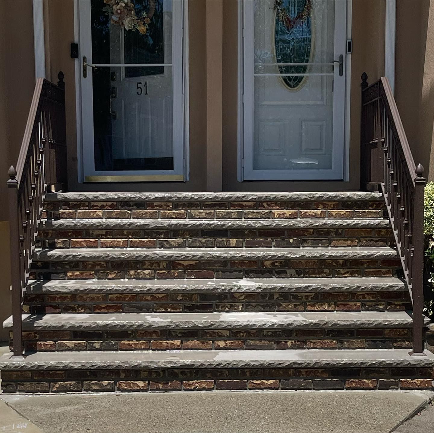 Five brick steps with concrete treads and dark metal railings lead up to two front doors, one marked with the number 51.