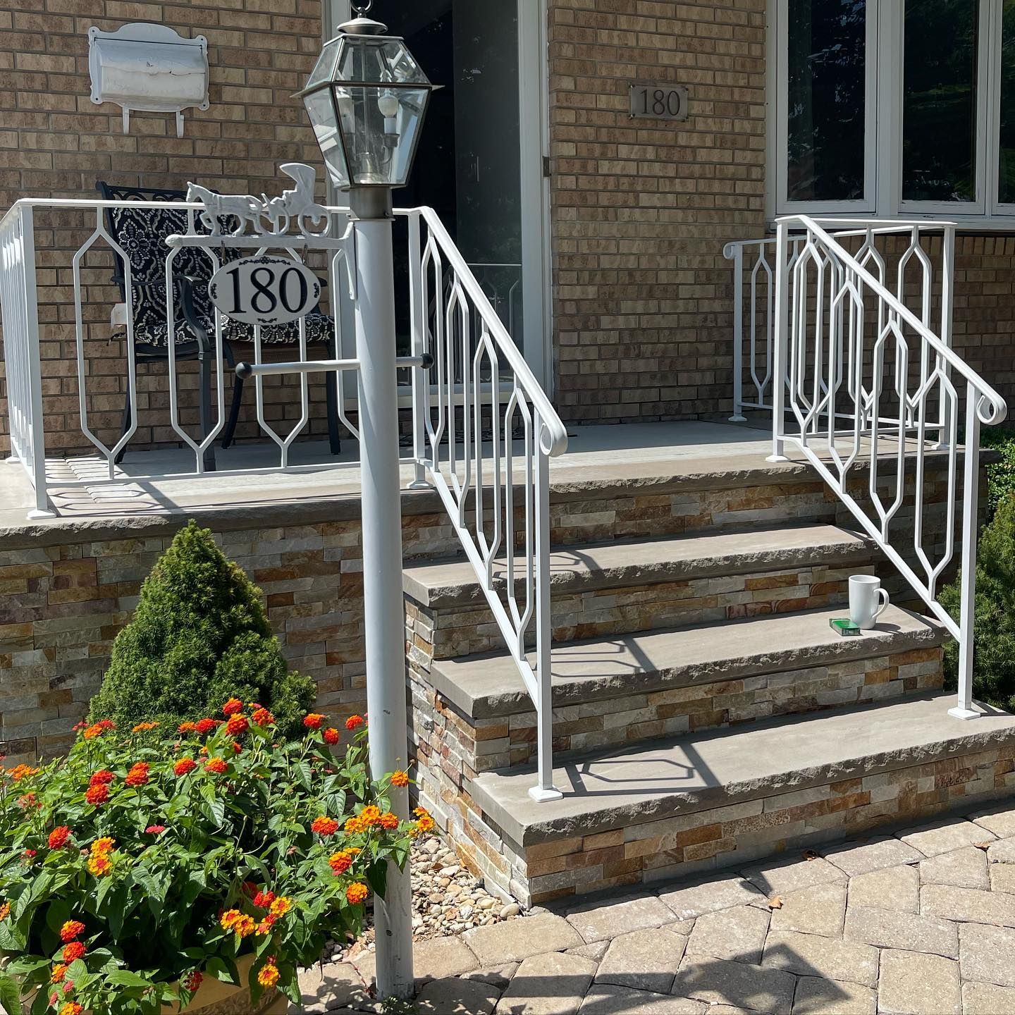 White metal railings frame stone steps leading to a brick home entrance with a house number 180 and a blooming planter.