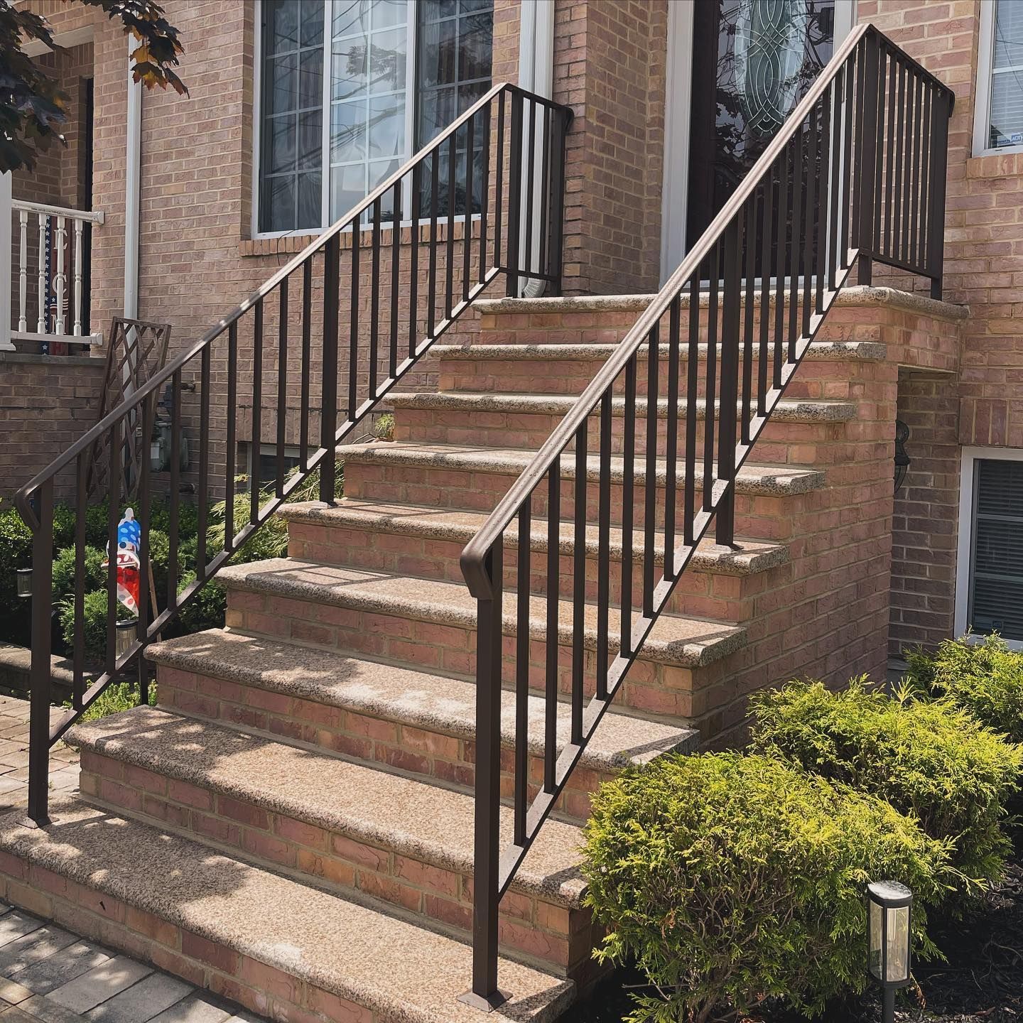 A tan brick house entrance with stone stairs and black metal railings leading up to the front door.