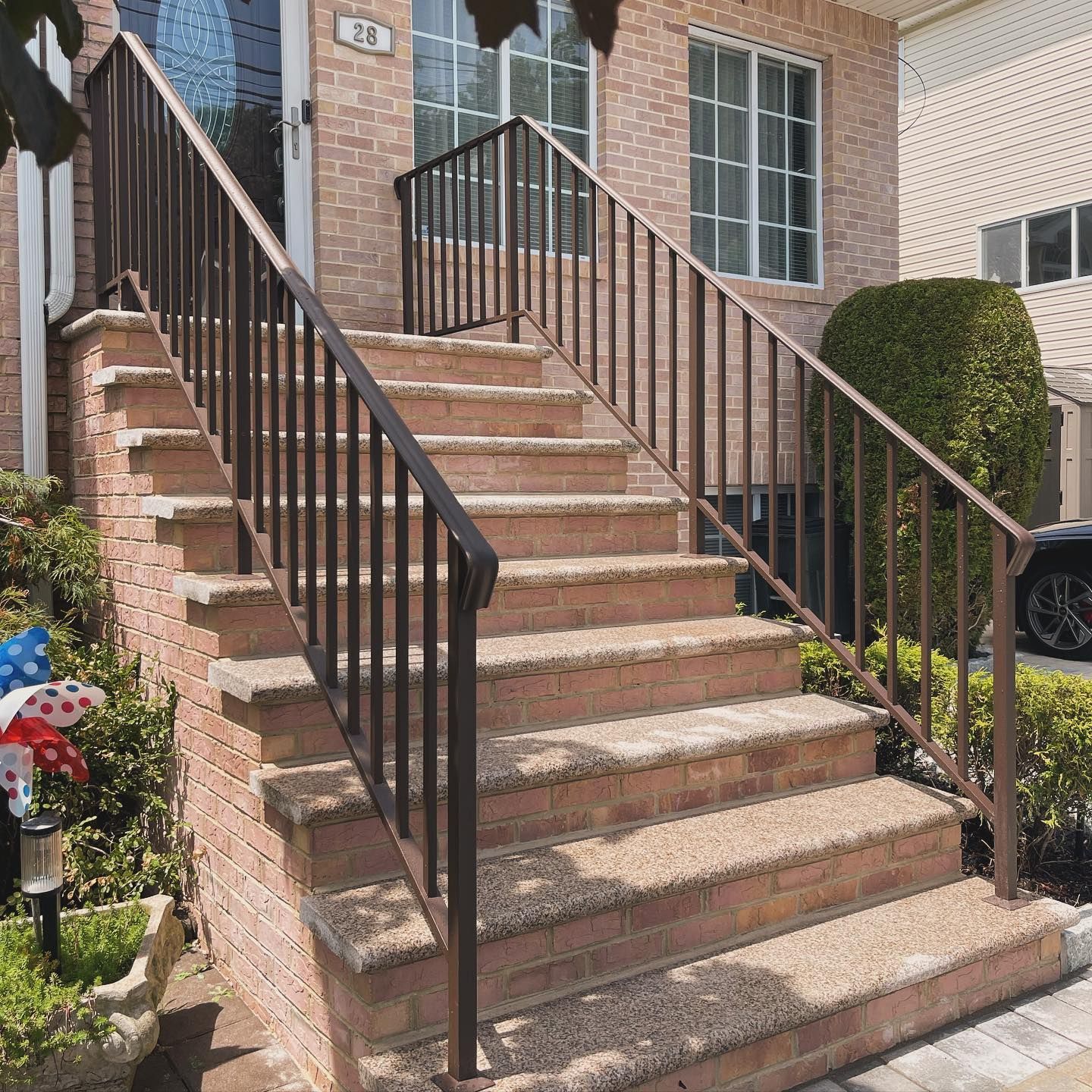Outdoor brick staircase leading to a front door, featuring textured stone-look steps and simple dark metal railings.