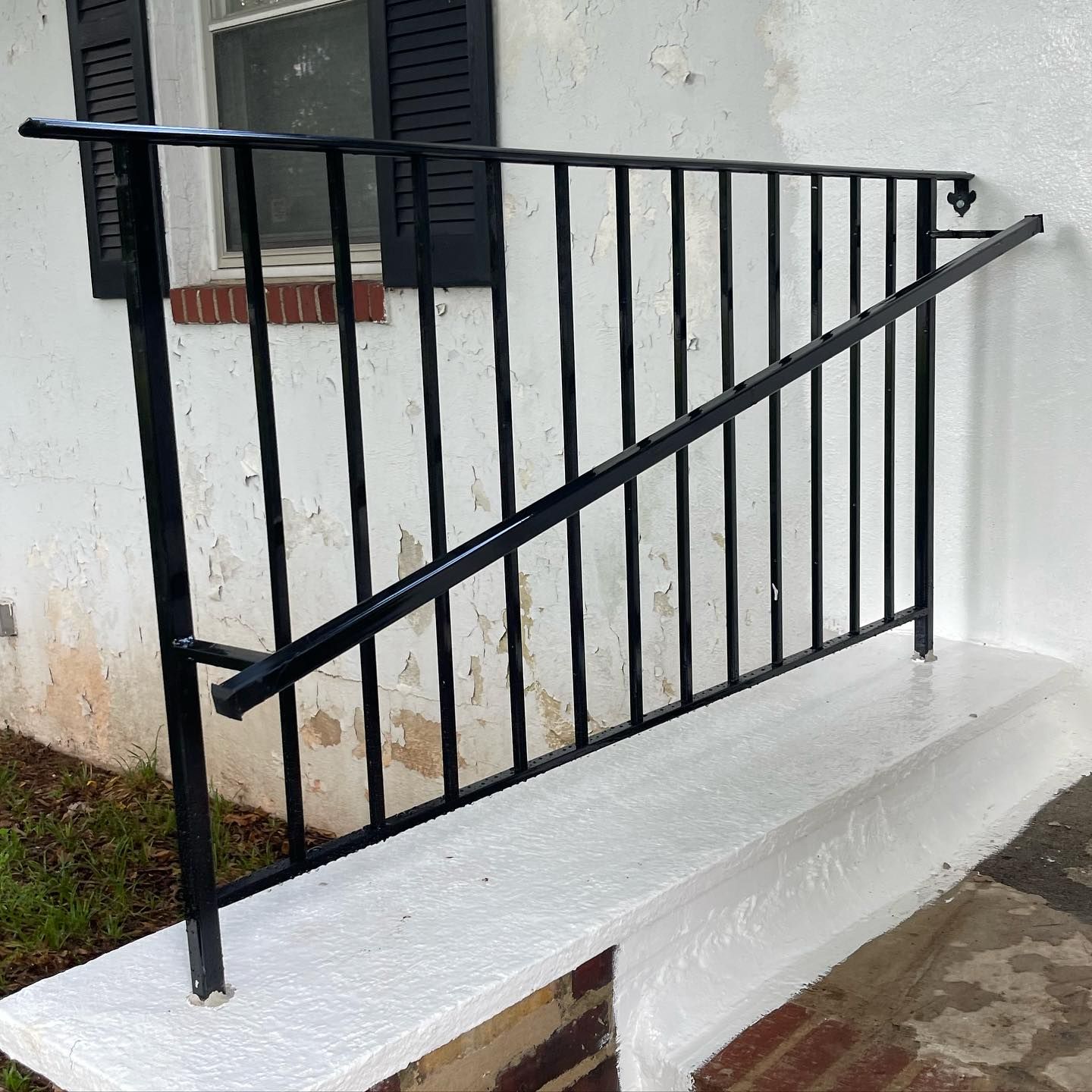 Black metal handrail and decorative railing mounted on a white painted concrete step against a white exterior wall.