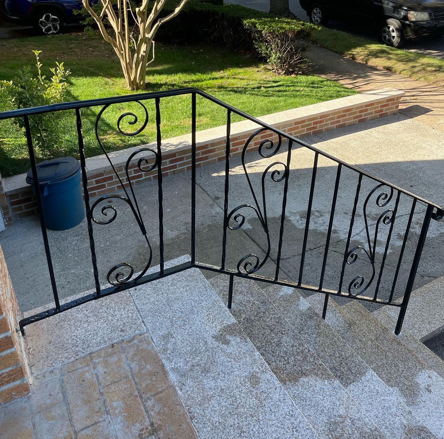 Black wrought iron railing with decorative scrollwork bordering a stone walkway and steps outside a house.