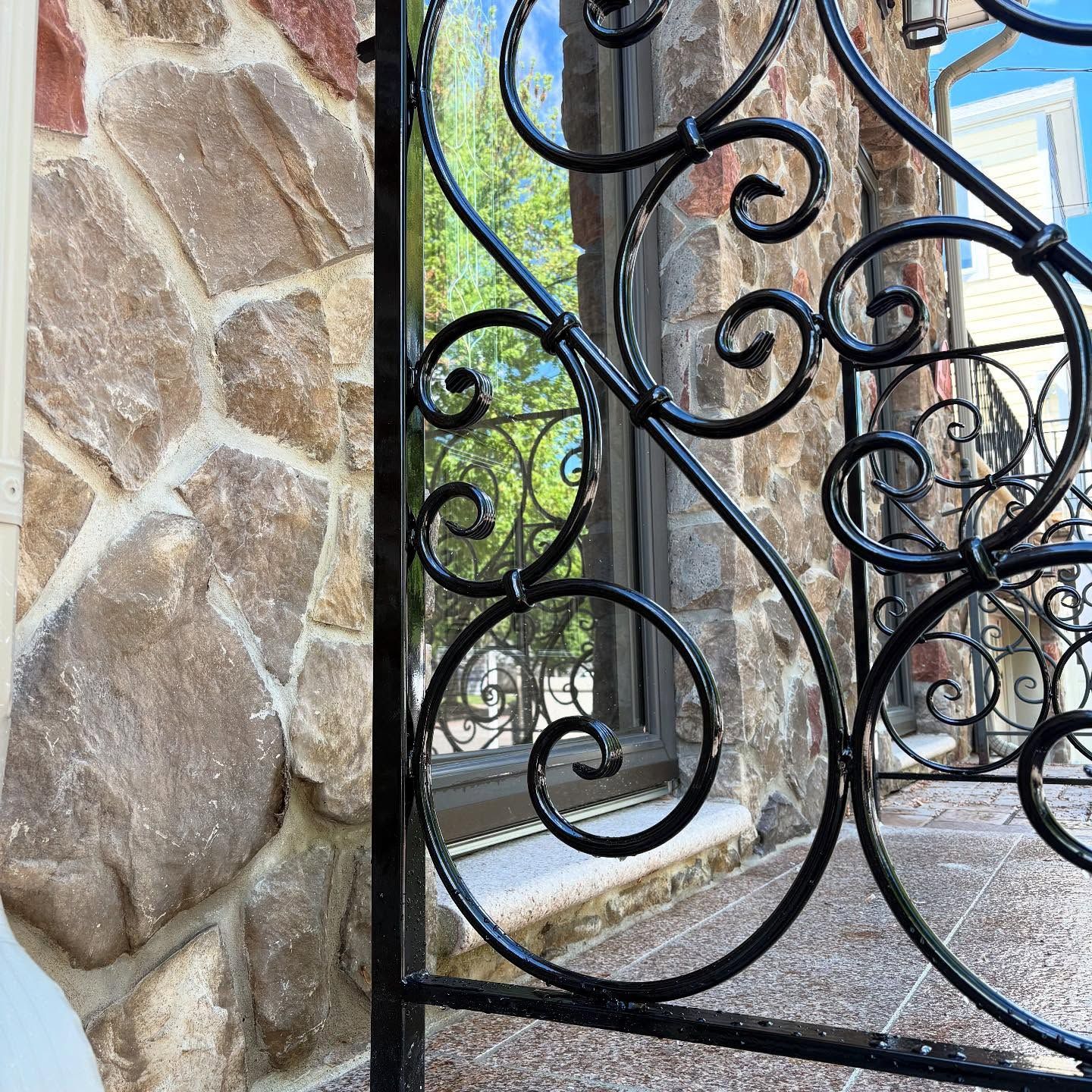 Black wrought-iron decorative railing with swirling scroll patterns set against a stone wall and a window.