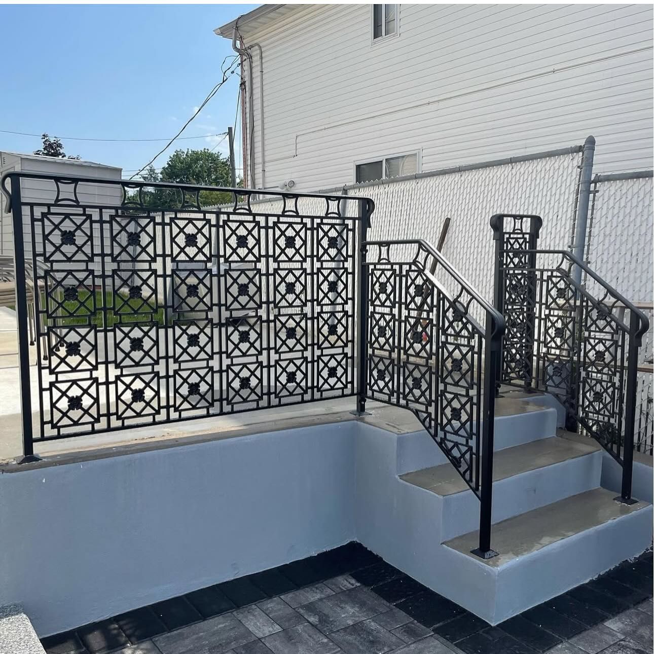 Black metal railing with a decorative grid pattern installed on light blue concrete stairs and a raised patio.