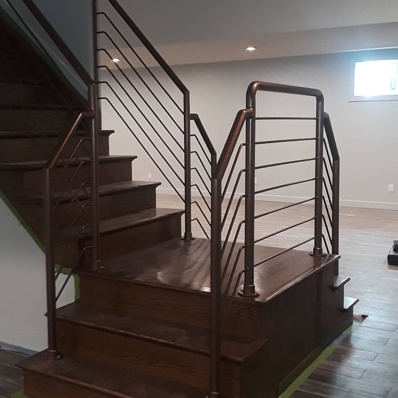 Dark-stained wooden staircase with bronze-colored metal railings and horizontal balusters in a modern home interior.