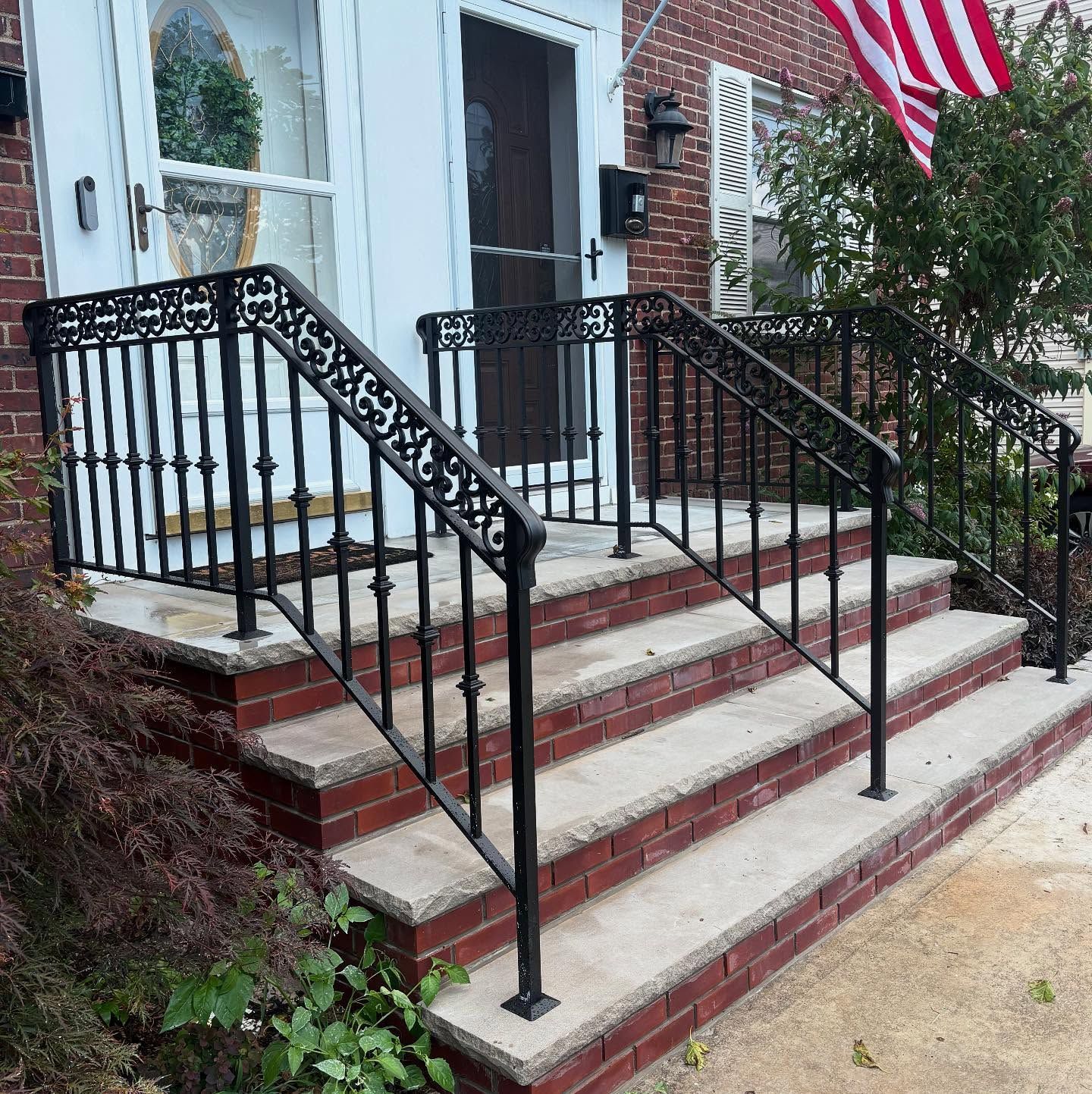 Concrete steps with red brick sides and black metal decorative railings leading to a white front door.
