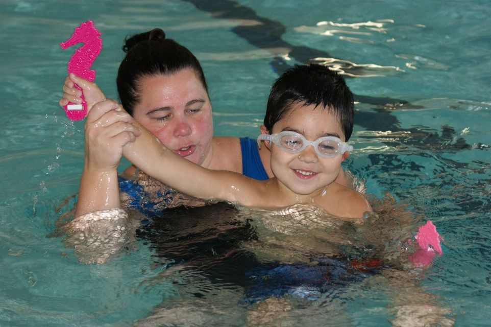 A woman is helping a young boy in a swimming pool.