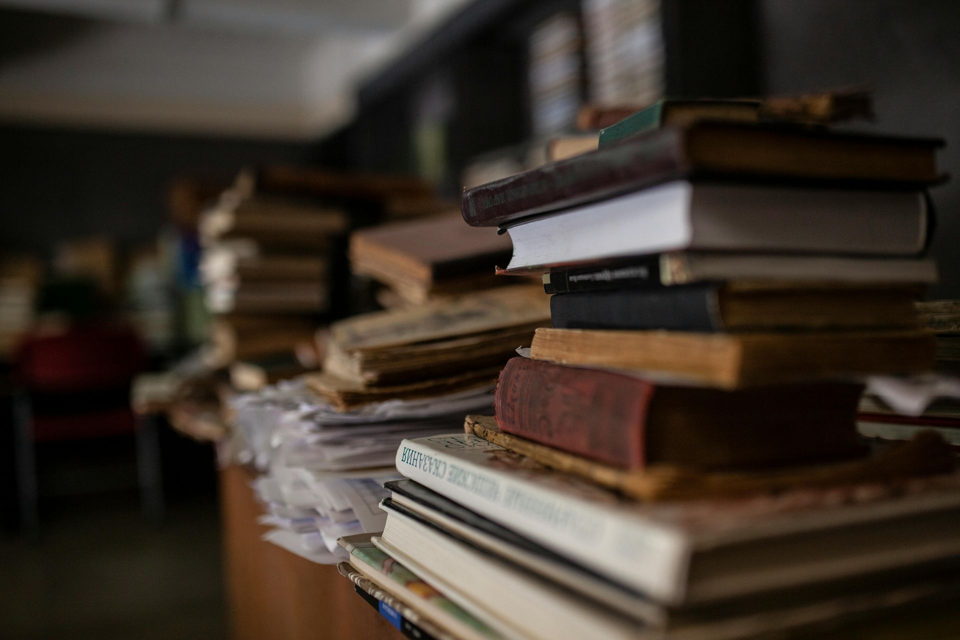 Stacks of old books piled on a table in a dimly lit room