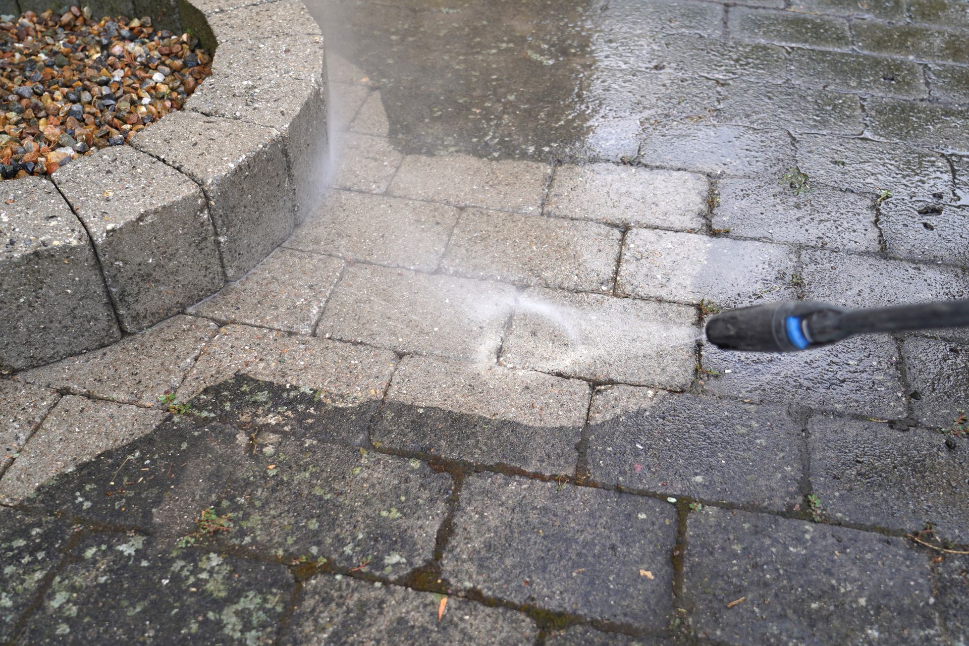 Nettoyage à haute pression d'une terrasse en briques ; jet d'eau près d'une jardinière en pierre.
