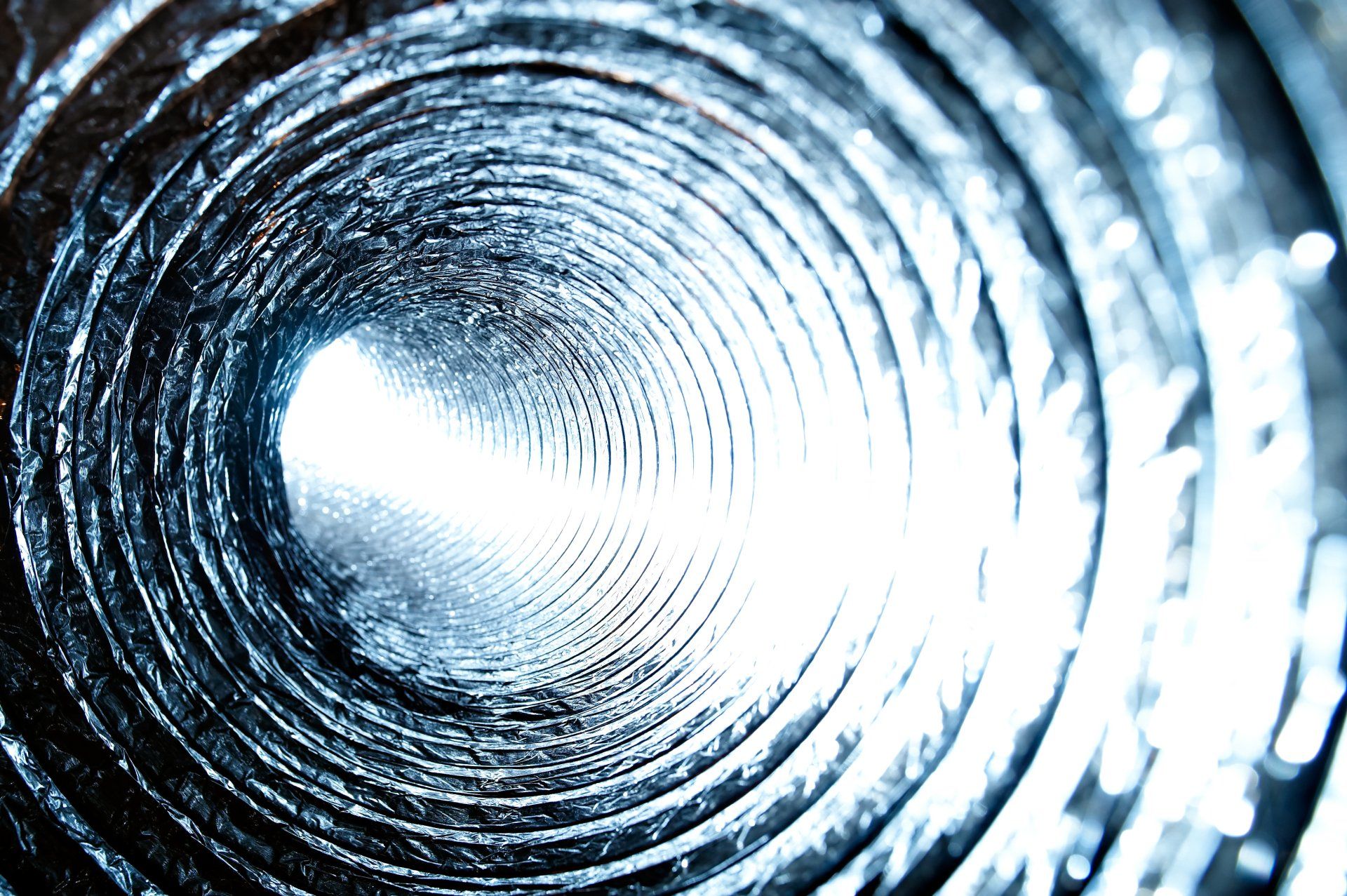 Vue intérieure d'un conduit métallique flexible, s'enroulant en spirale vers une lumière vive à son extrémité.