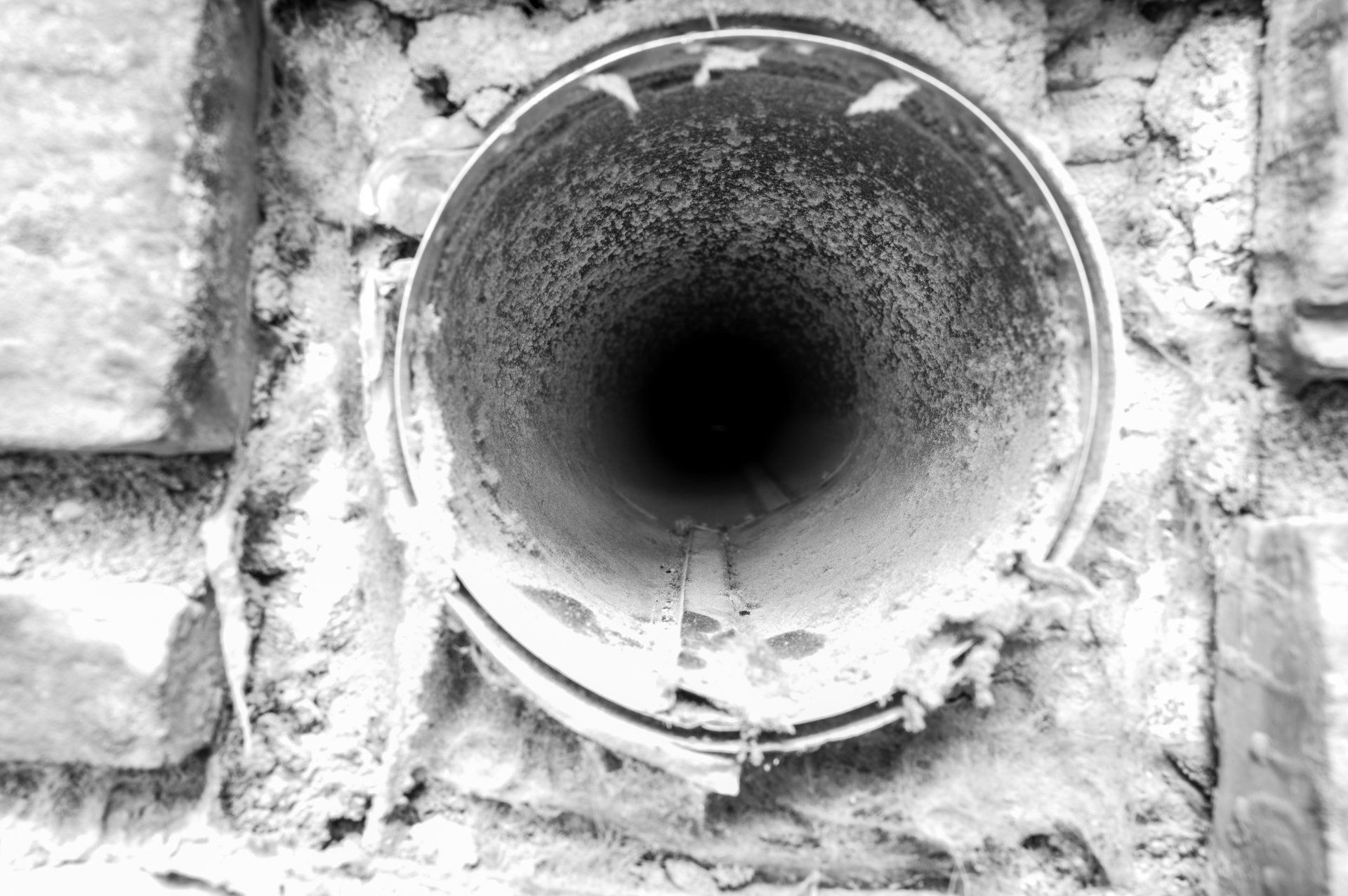 Vue intérieure d'un conduit métallique recouvert de poussière et de débris, encastré dans un mur de briques.