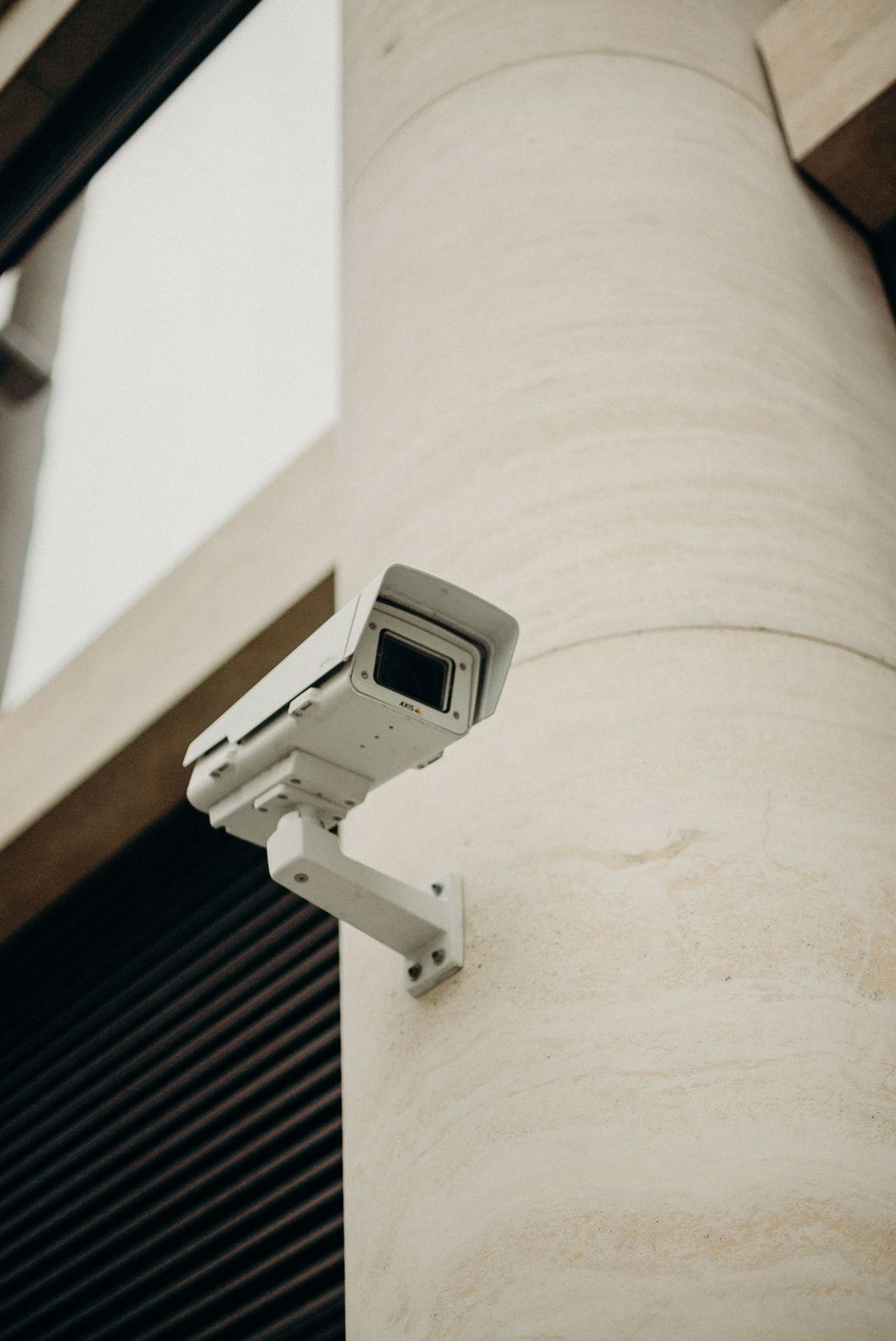 Telecamera di sicurezza montata su una colonna beige dell'edificio, inclinata verso il basso all'esterno.