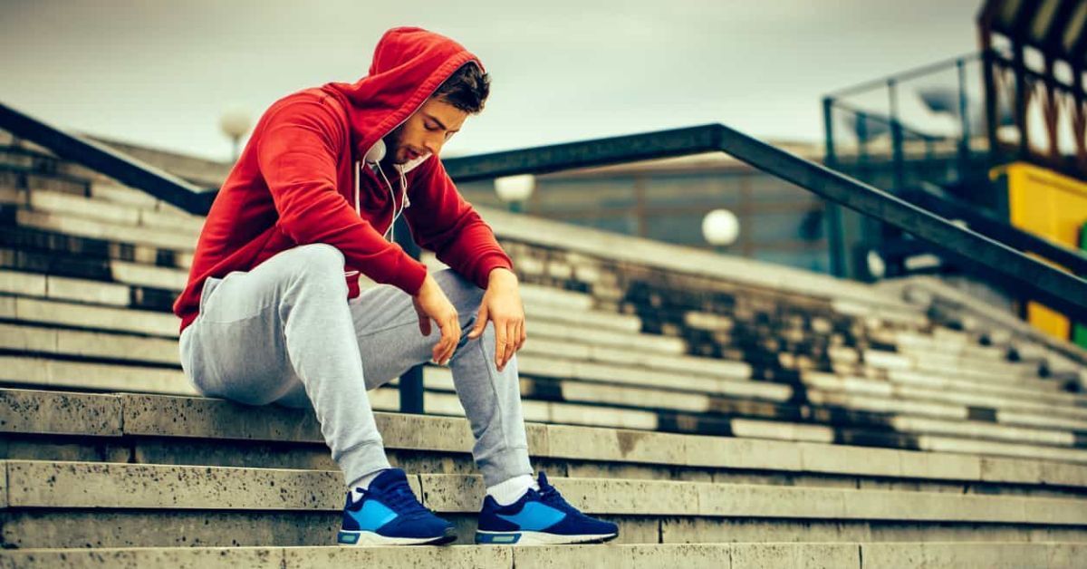 A man in a red hoodie is sitting on a set of stairs.