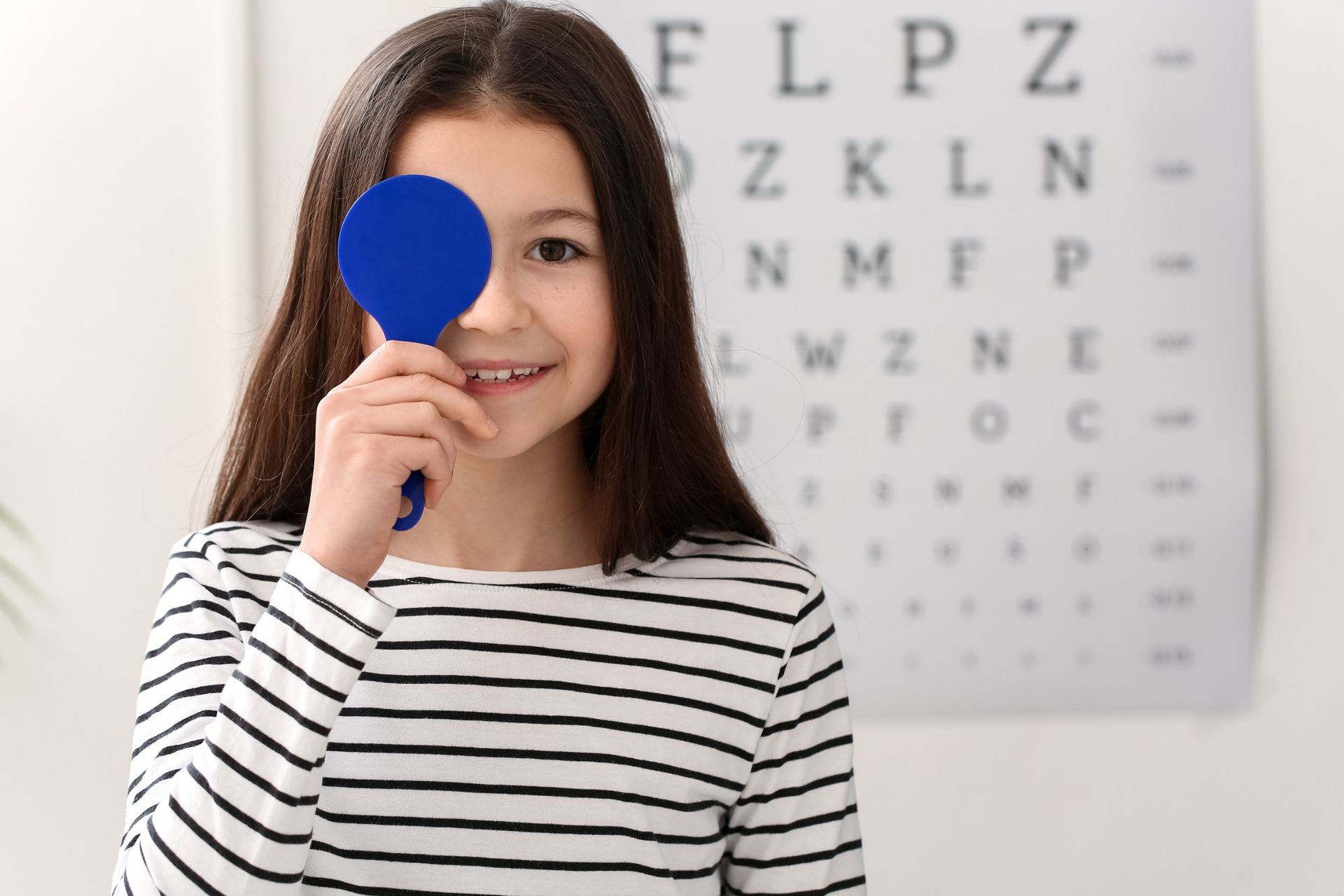 A young girl is holding a blue mirror in front of her eye.