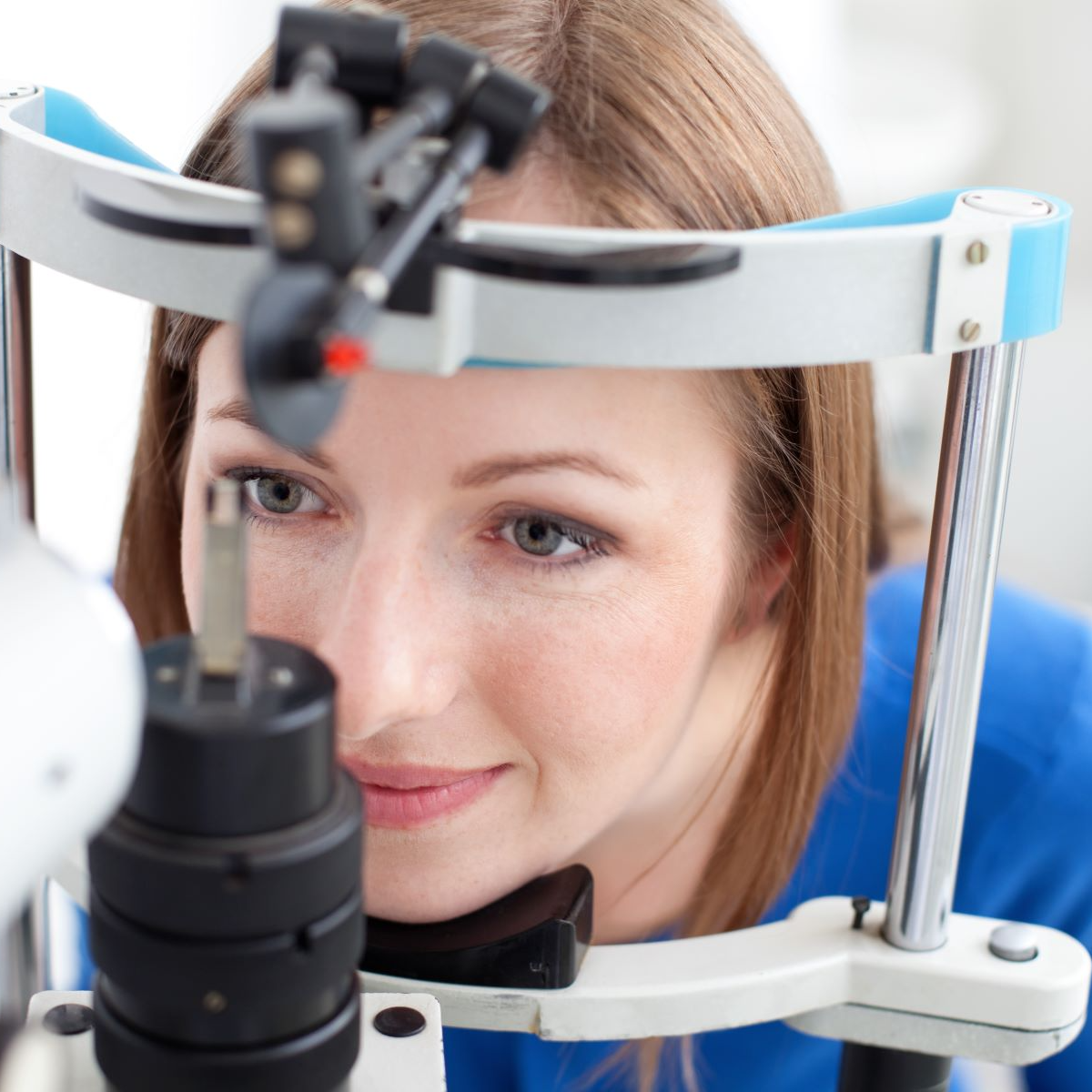 A woman in a blue shirt is looking through a microscope