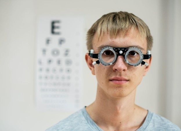 A man wearing glasses is standing in front of an eye chart.