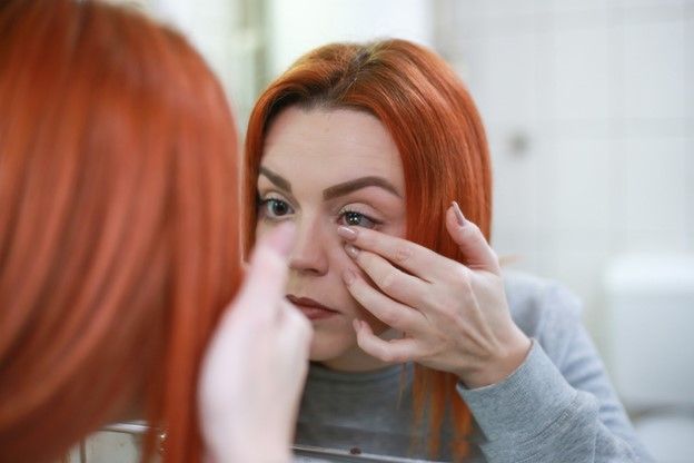 A woman with red hair is looking at herself in the mirror.