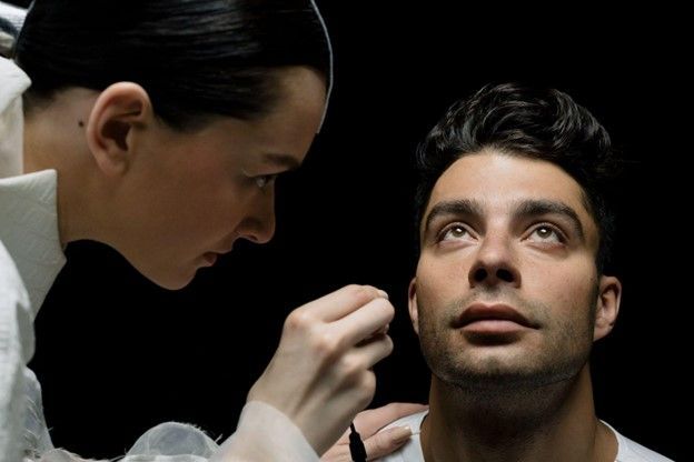 A woman is applying makeup to a man 's face.
