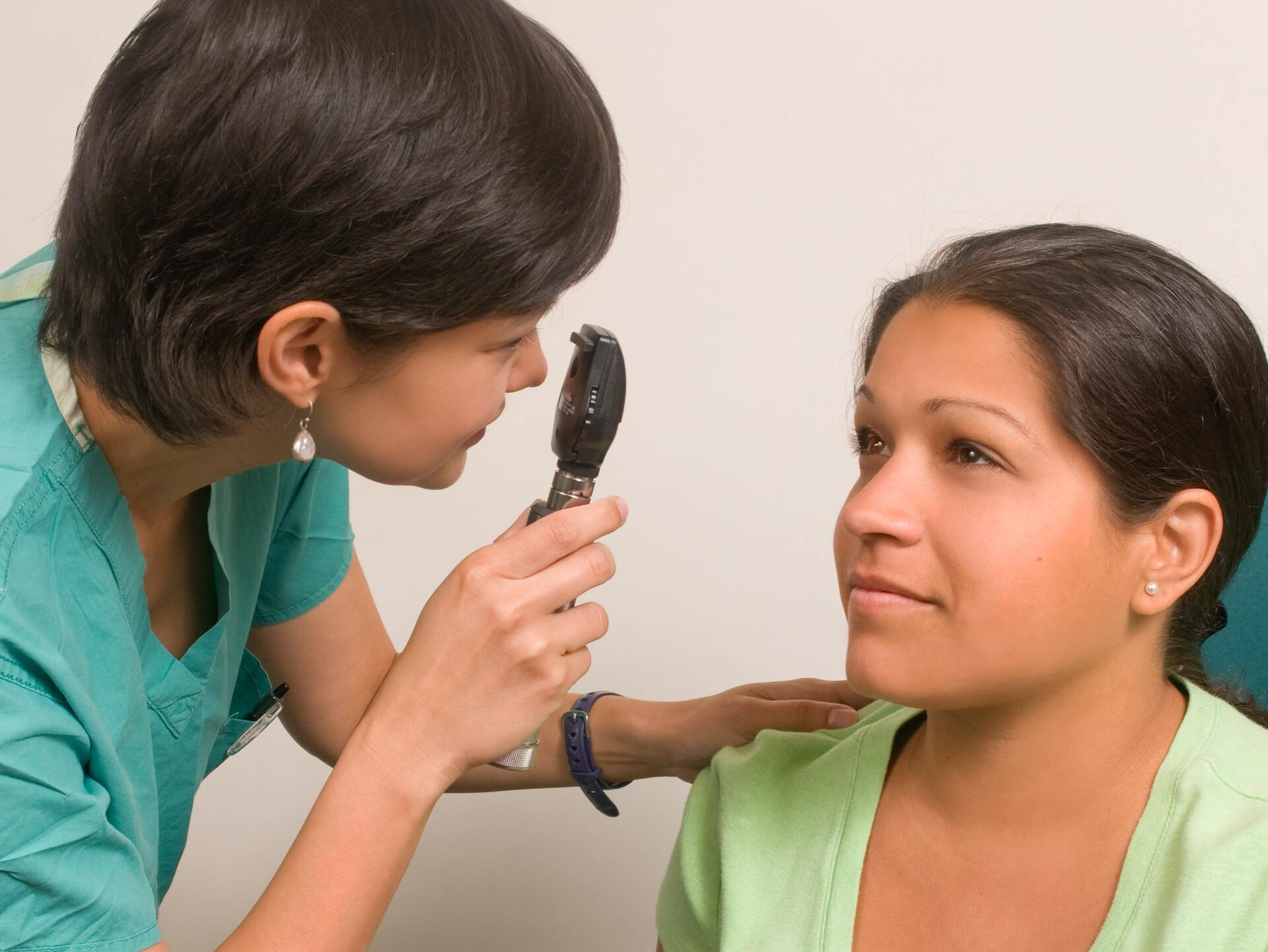 A nurse examines a woman 's eye with an ophthalmoscope
