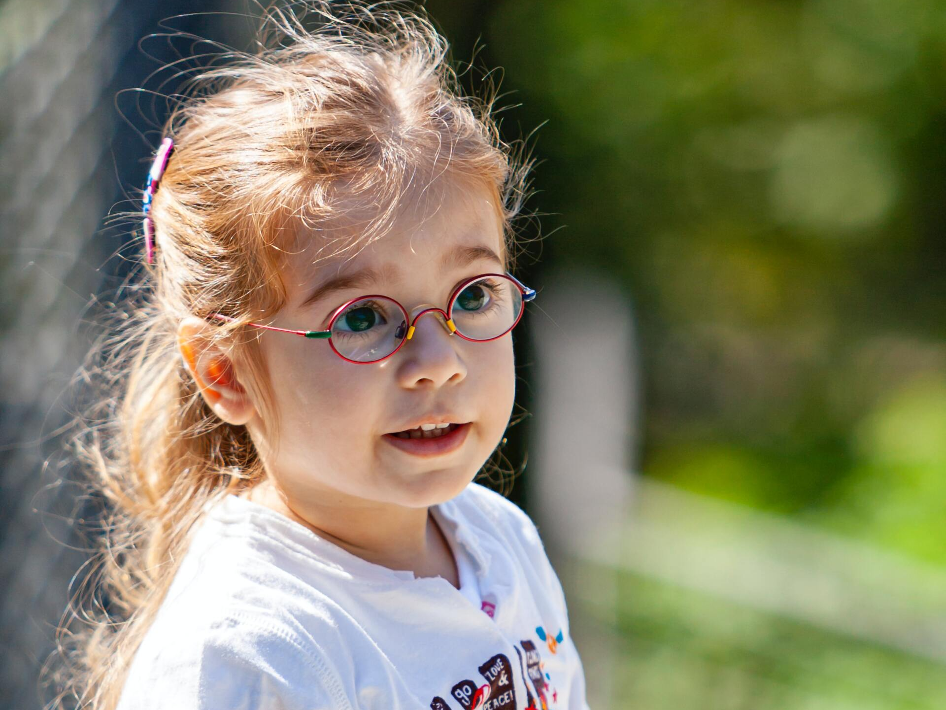 A little girl wearing glasses and a white shirt is looking at the camera.
