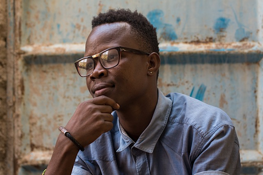 A man wearing glasses is sitting down with his hand on his chin.
