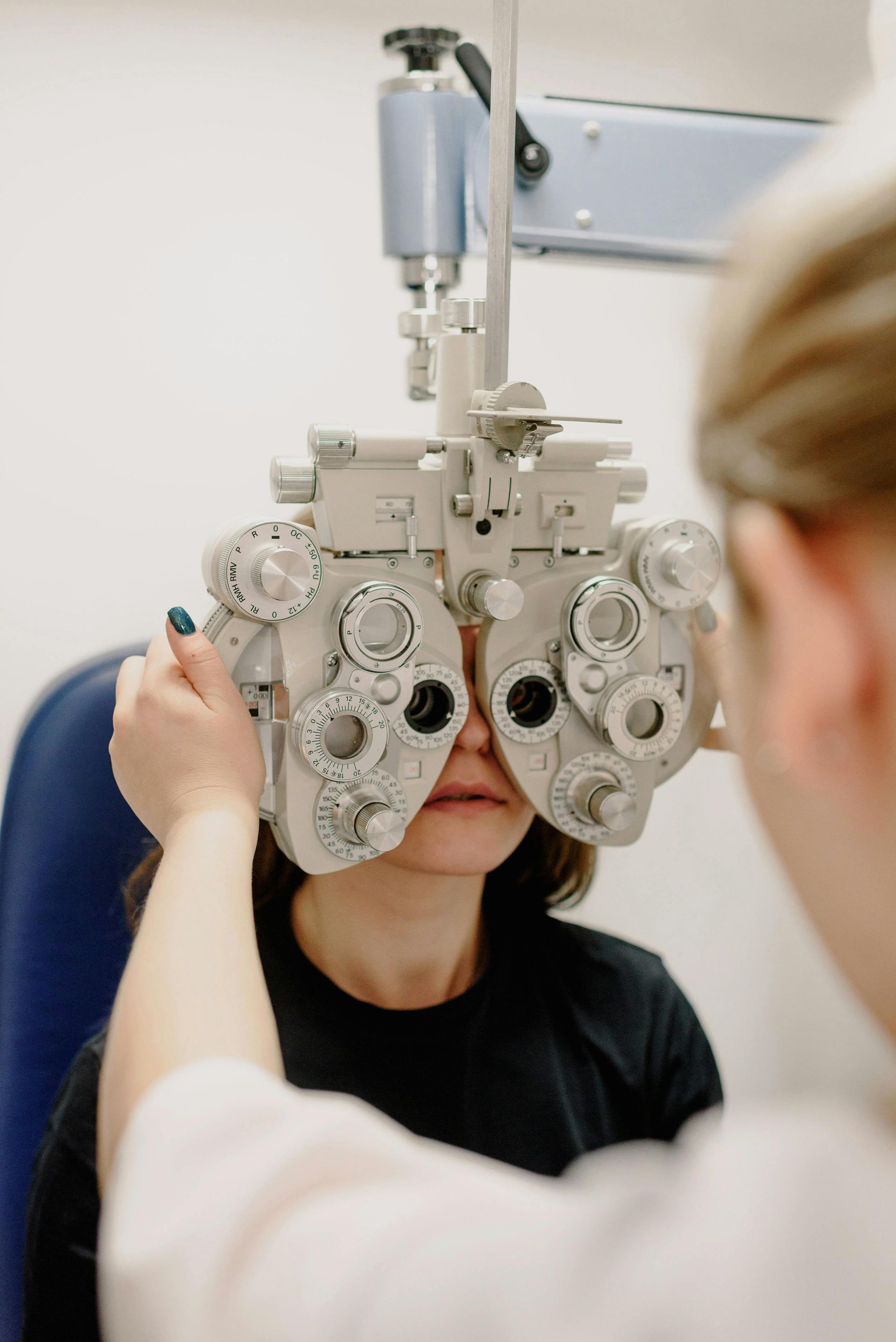 Person undergoing an eye exam using a phoropter in an exam room.