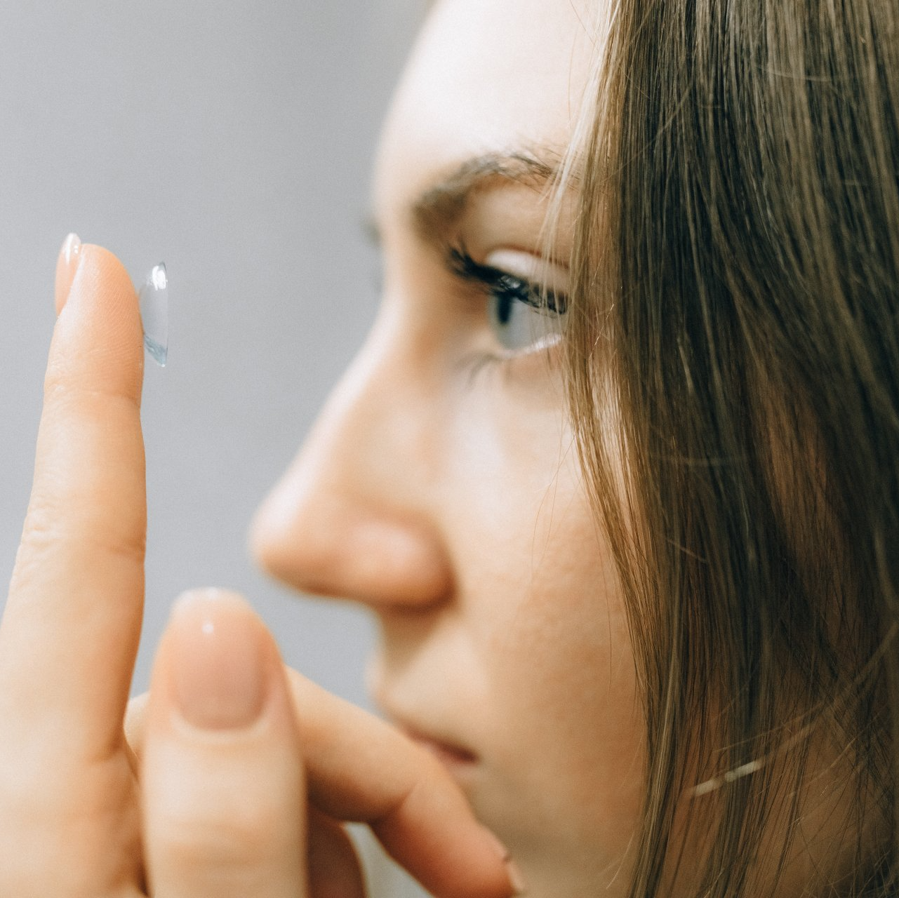 A woman is putting a contact lens on her finger.