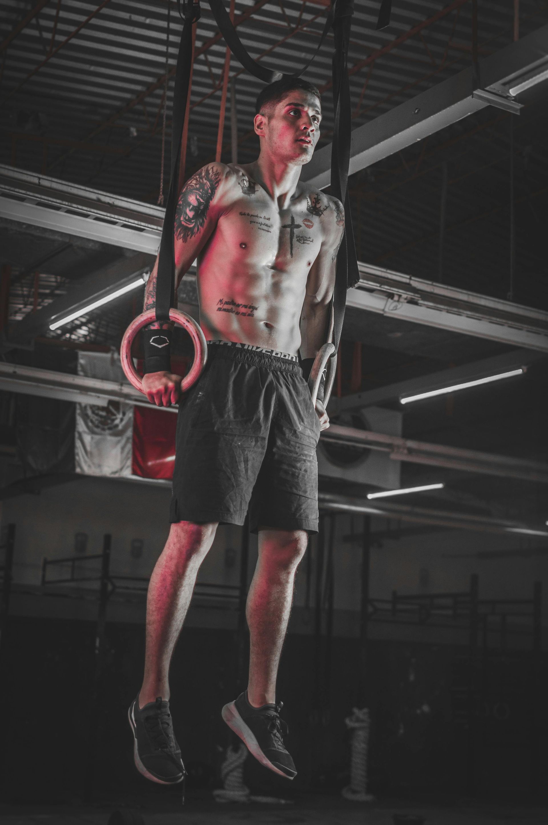 A shirtless man is doing dips on gymnastic rings in a gym.