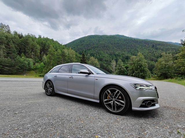 Silver sedan parked on gravel beside a forested mountain road under cloudy skies