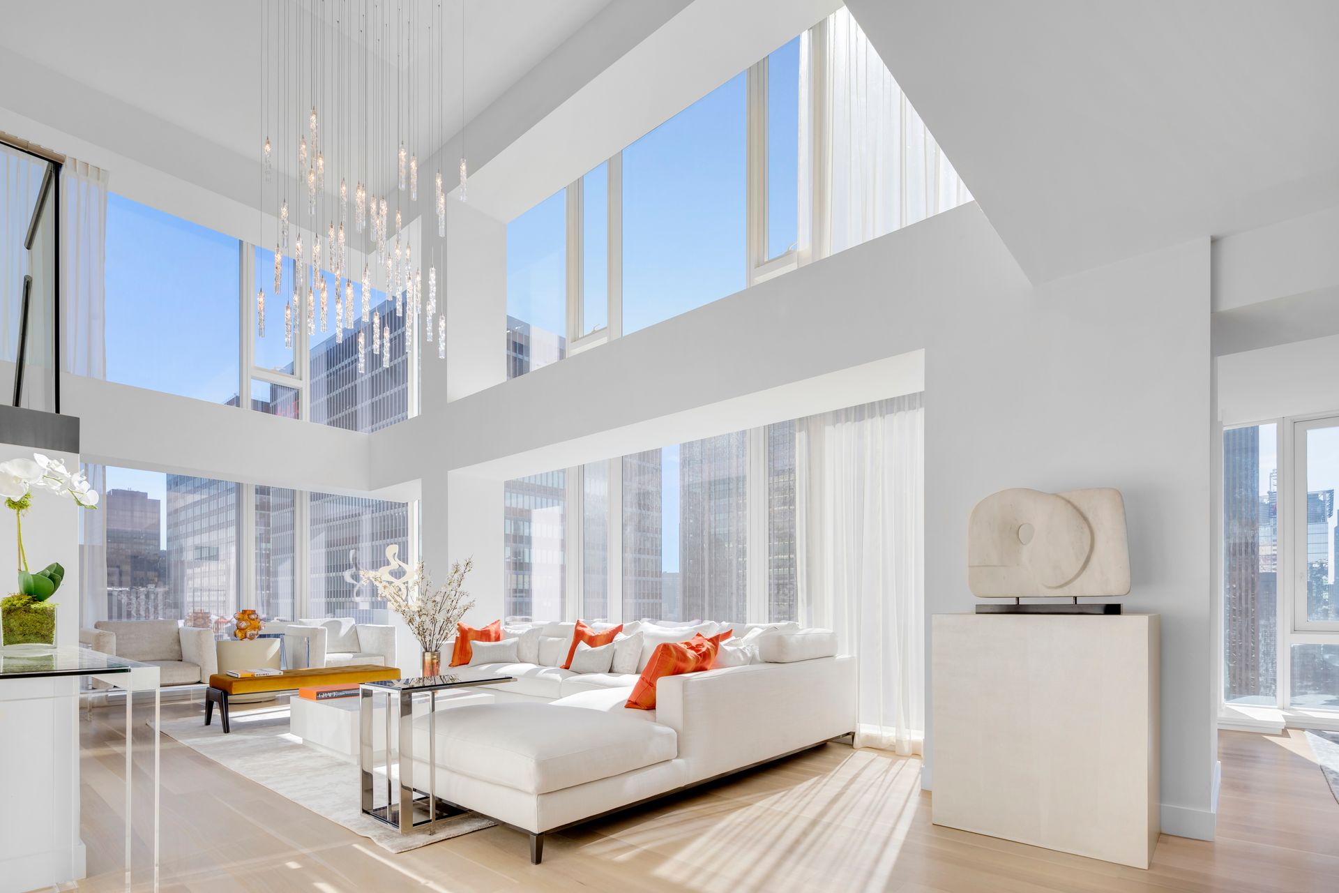 Bright modern living room with white furniture, orange accents, and floor-to-ceiling windows