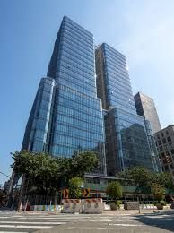 Modern glass office towers with blue-tinted windows under a clear sky, seen from street level