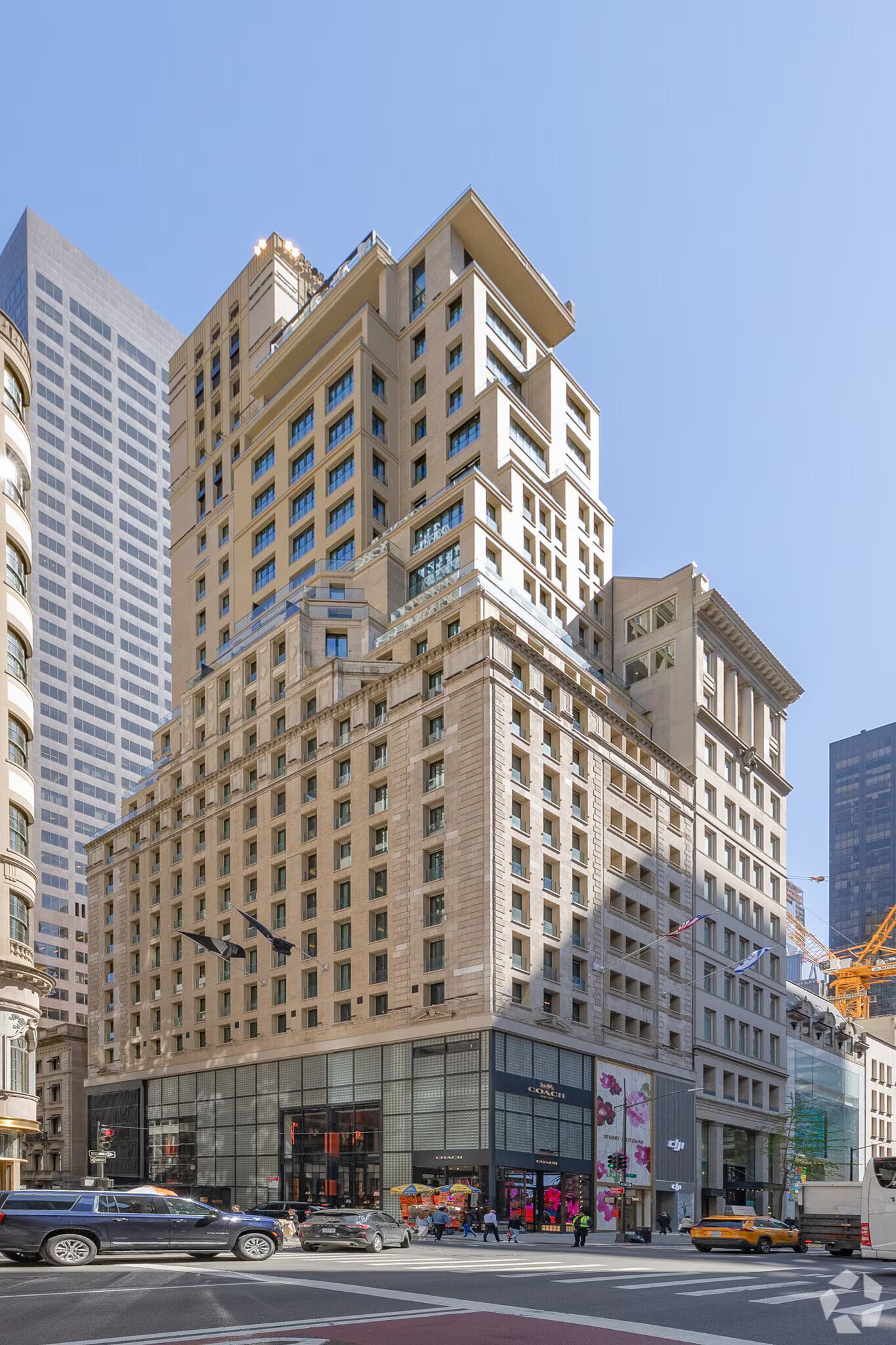 Tall beige high-rise building on a city street under a clear blue sky