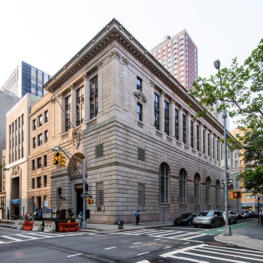 Historic stone building on a city corner with arched windows, street traffic, and tall modern buildings behind