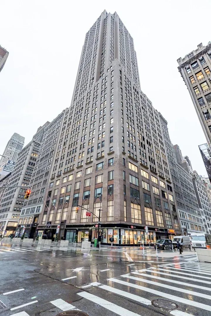 Tall gray skyscraper at a city intersection on a wet, snowy street with crosswalks and surrounding buildings