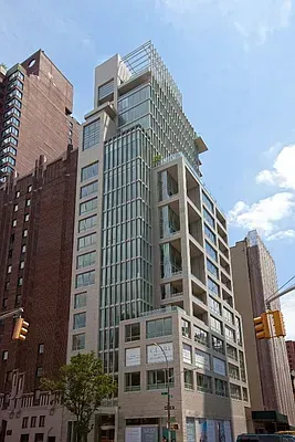 Tall modern glass-and-concrete building on a city street under a partly cloudy sky.
